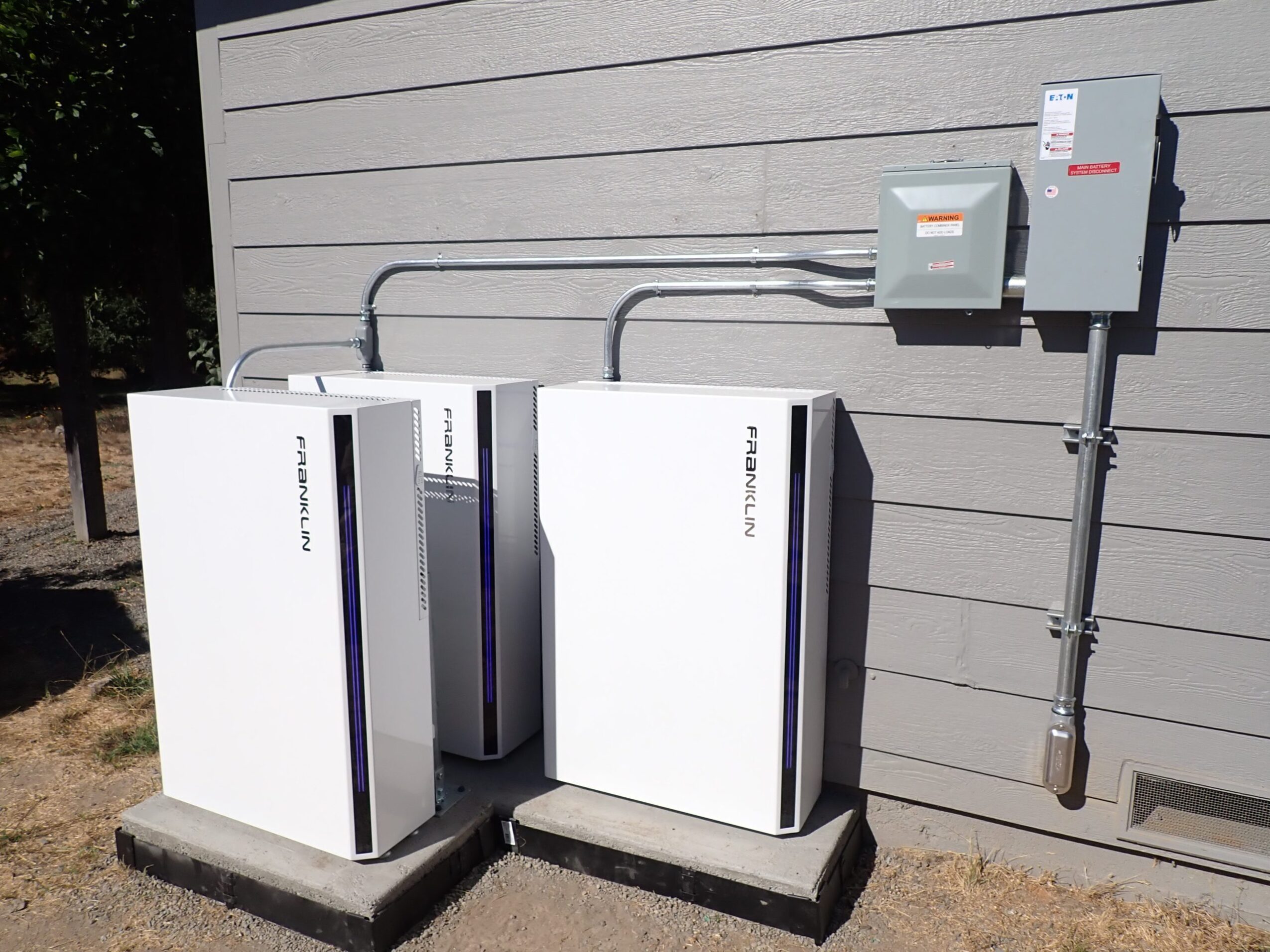 Three white electrical cabinets on concrete bases against a gray wall, with electrical boxes and conduit above.
