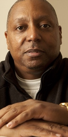 Close-up of a person with short hair, wearing a black jacket and white shirt, looking at the camera.