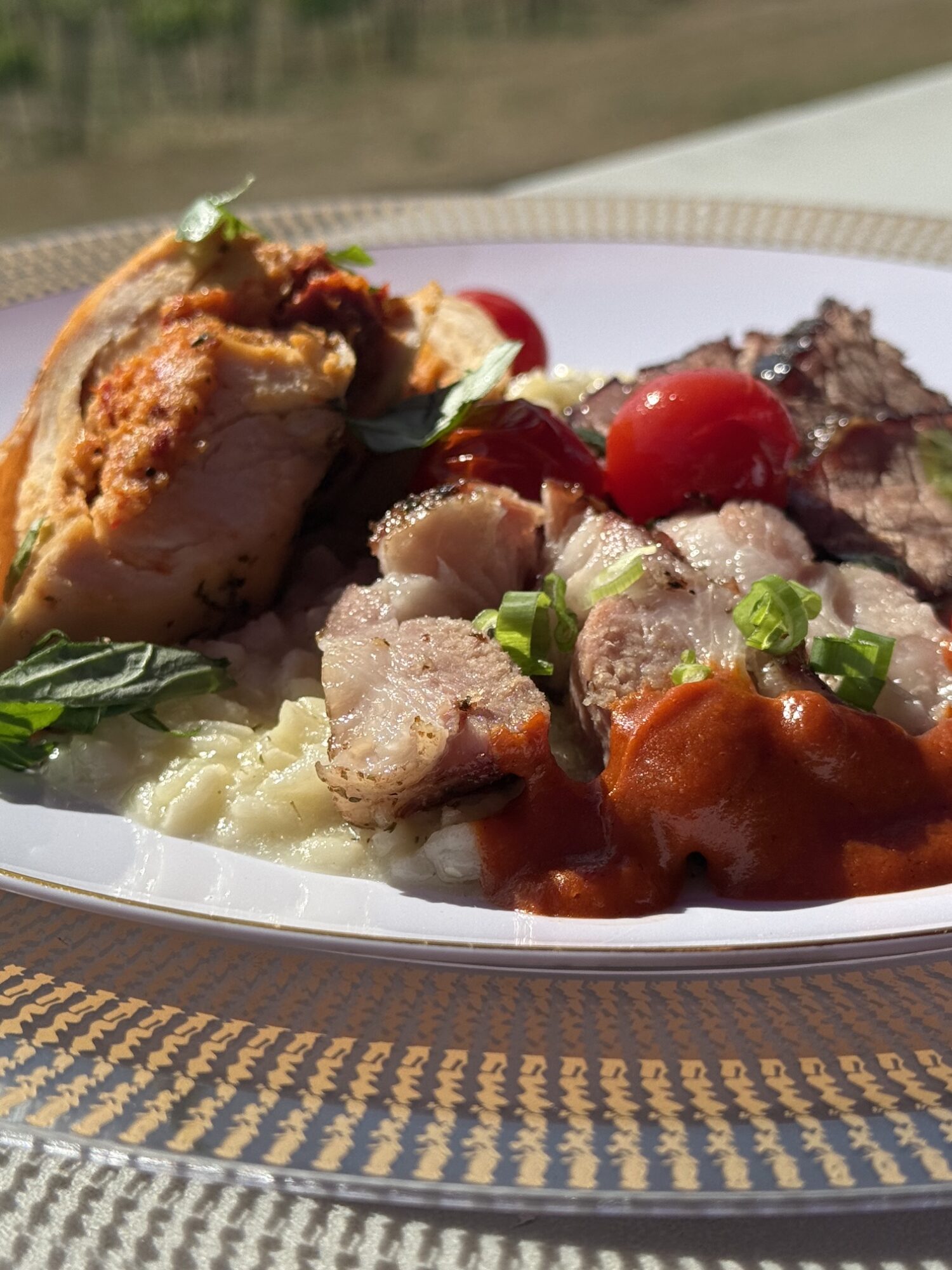 Plate with mashed potatoes, fried chicken, meat with vegetables, cherry tomatoes, and green garnish on a patterned surface.