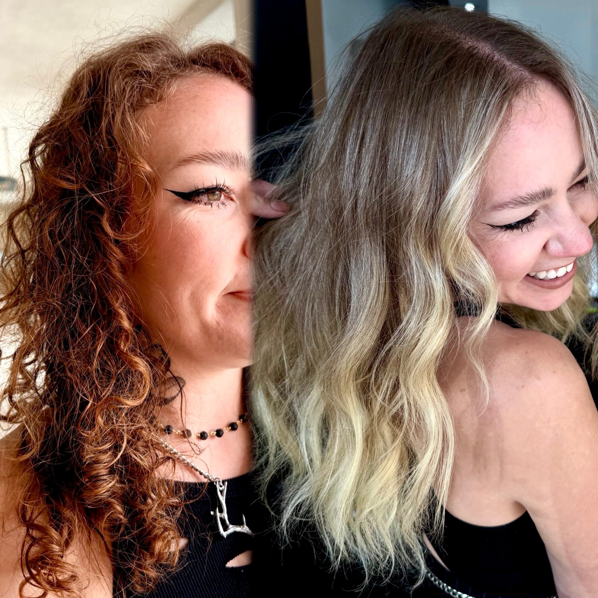 Two women smiling and laughing close together, one with curly red hair and the other with wavy blonde hair.