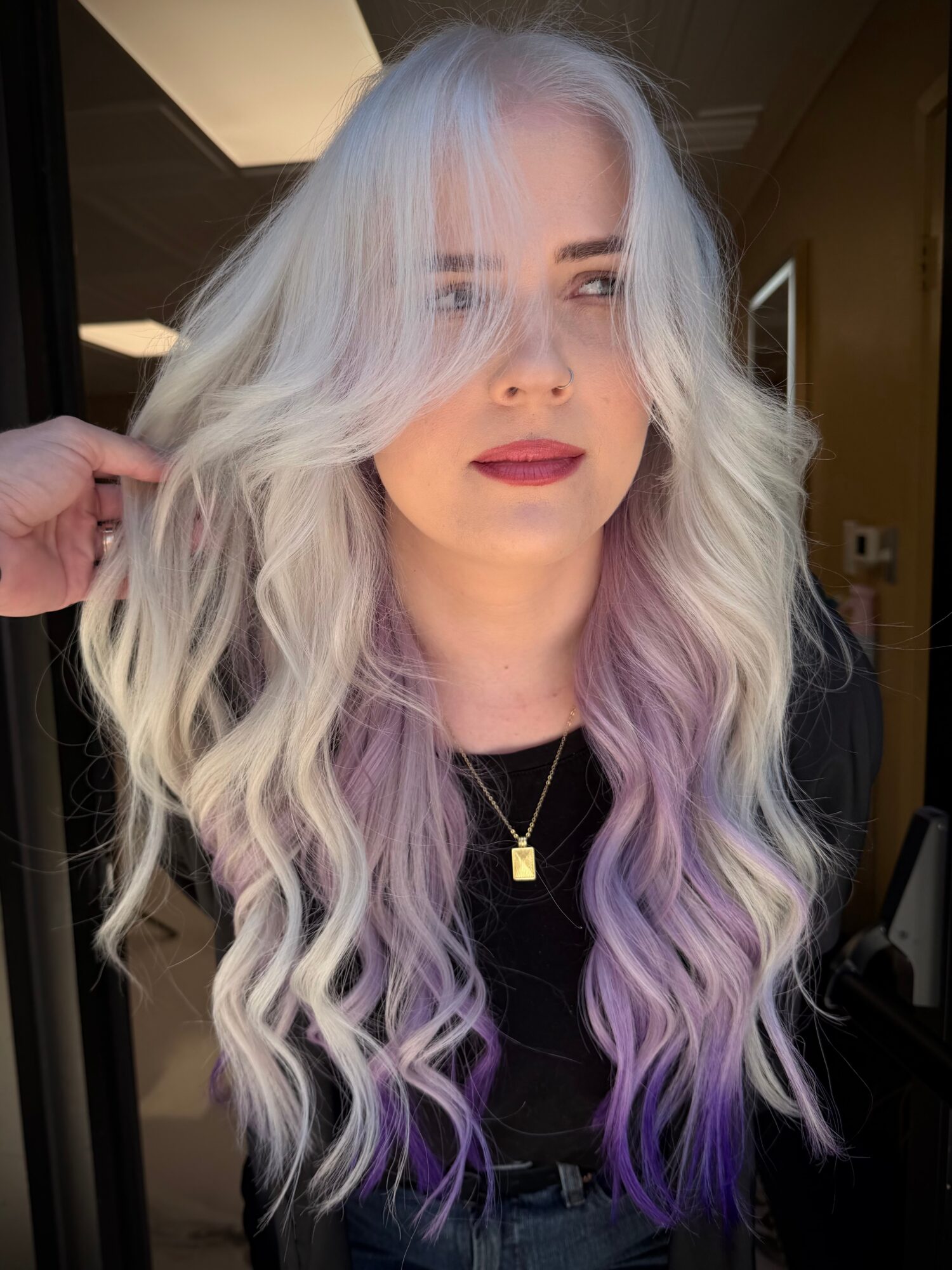 Woman with long, wavy hair dyed in pastel shades of blue, lavender, and purple, wearing a black top and gold necklace.