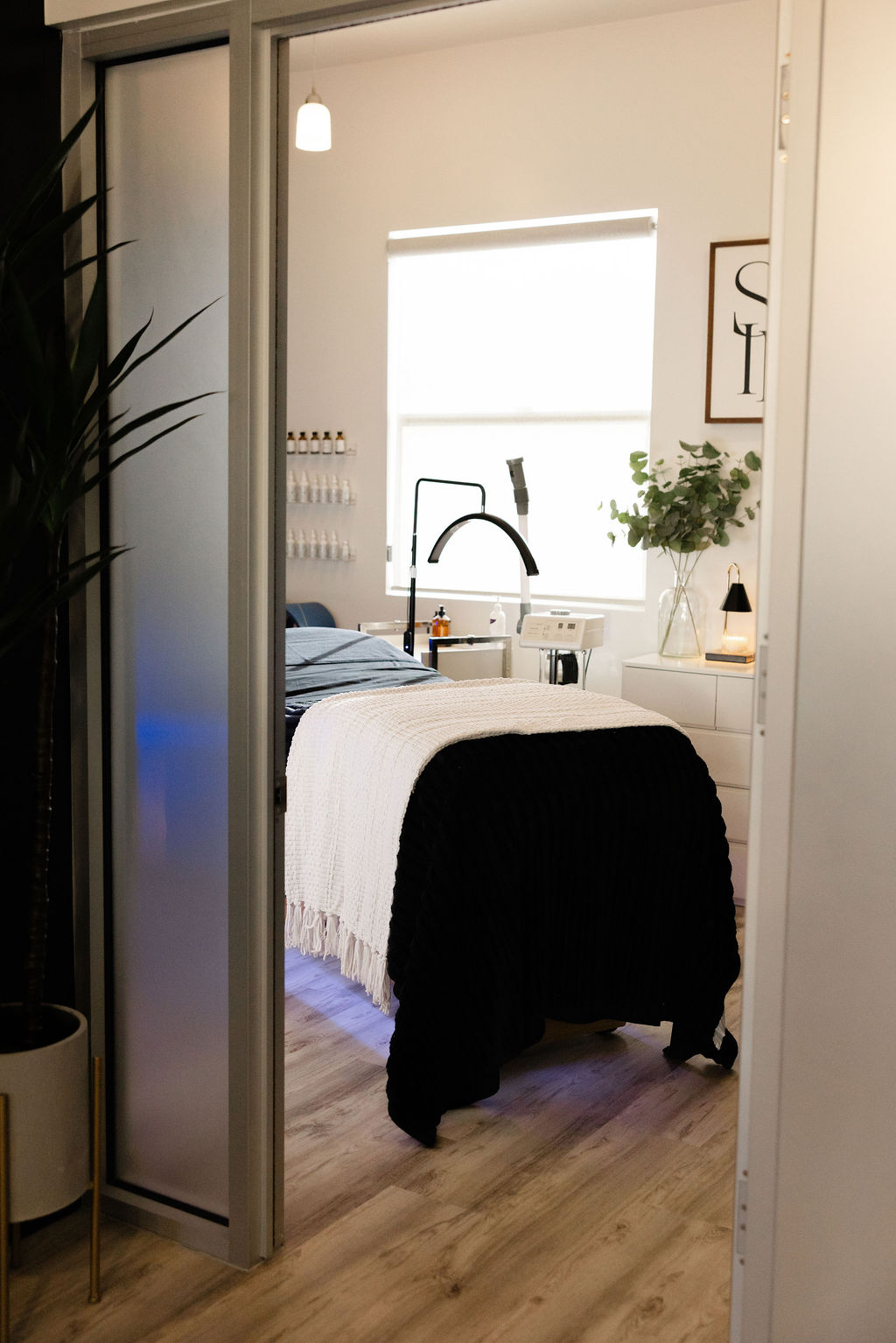 Bedroom with a bed, window, and plants, seen through a partially open sliding door.