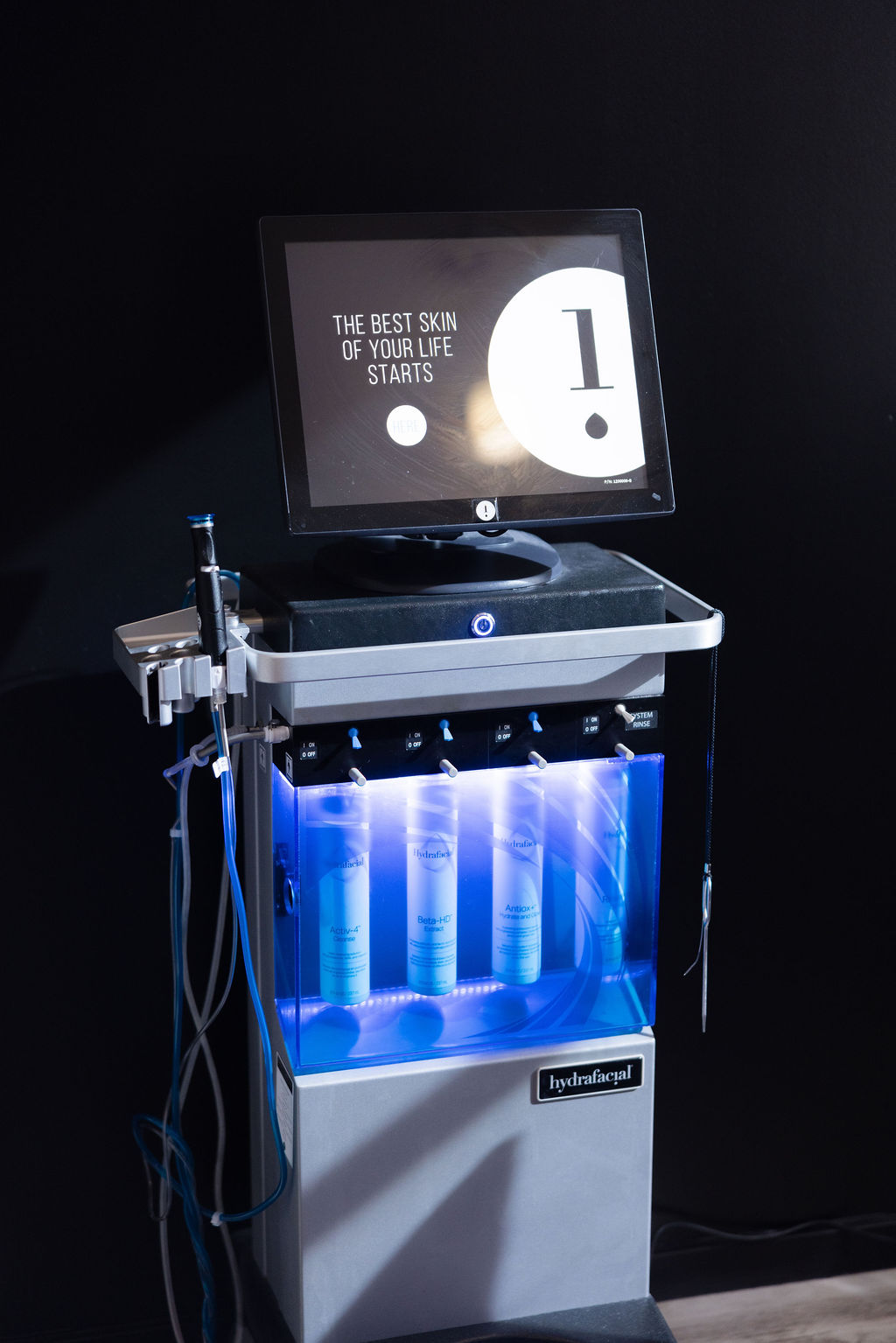 Medical or skincare device with a monitor displaying text and a number, illuminated blue lights inside, against a dark background.