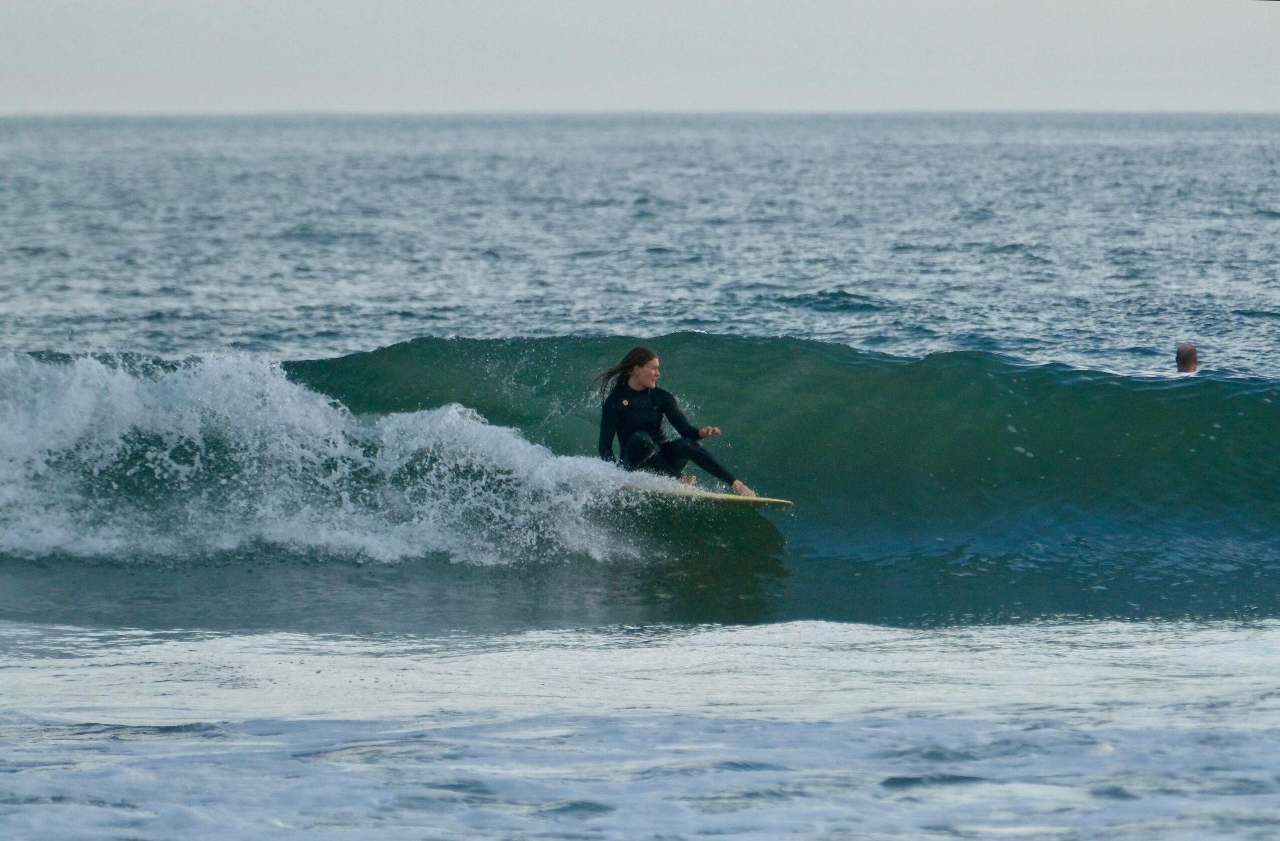 Person surfing on a wave in the ocean with another person in the background, overcast sky, ocean horizon
