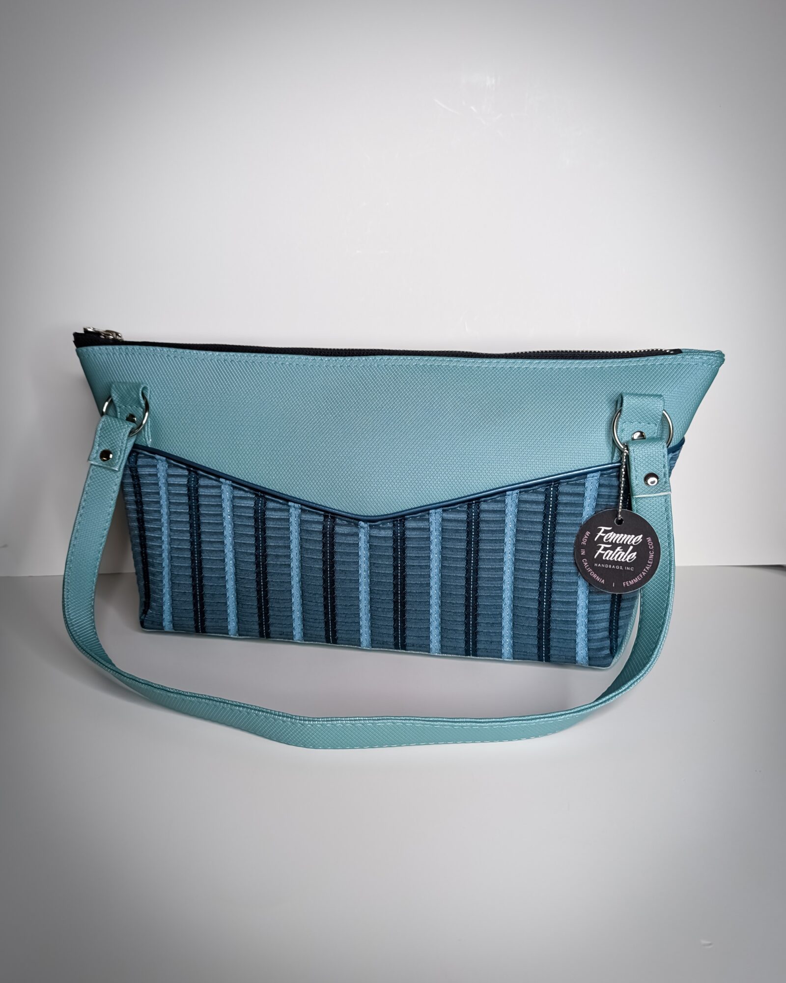 Light blue and dark blue striped fabric bag with a strap and a round tag, against a plain background.