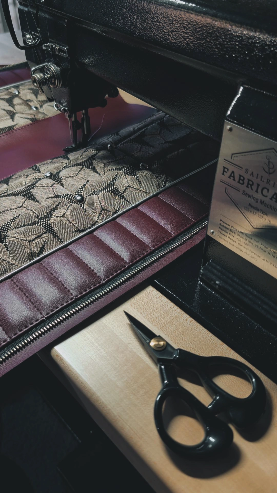 Sewing machine with fabric and scissors on a wooden surface, partially visible. The fabric has a snake pattern and a quilted border.