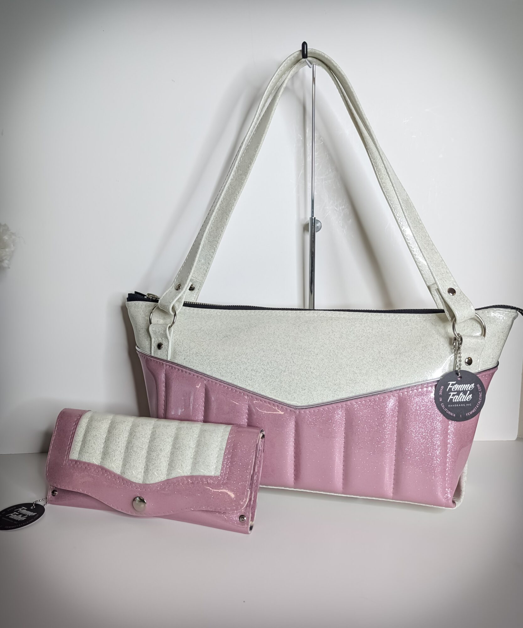 A white and pink tote bag with a smaller matching pouch, hanging on a wall hook against a plain background.