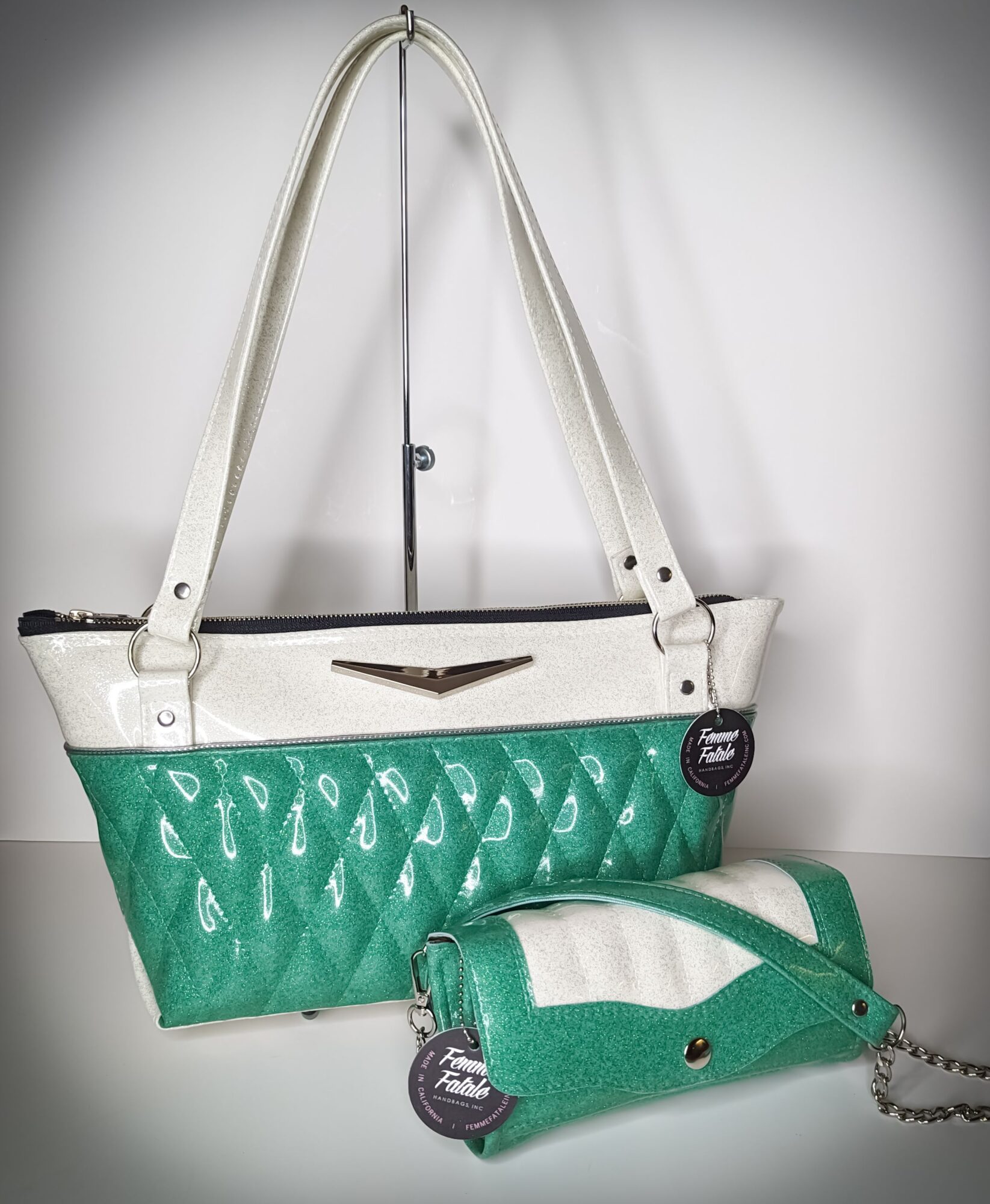 Green and white handbag with a smaller matching pouch, both hanging on a wall, with tags attached.