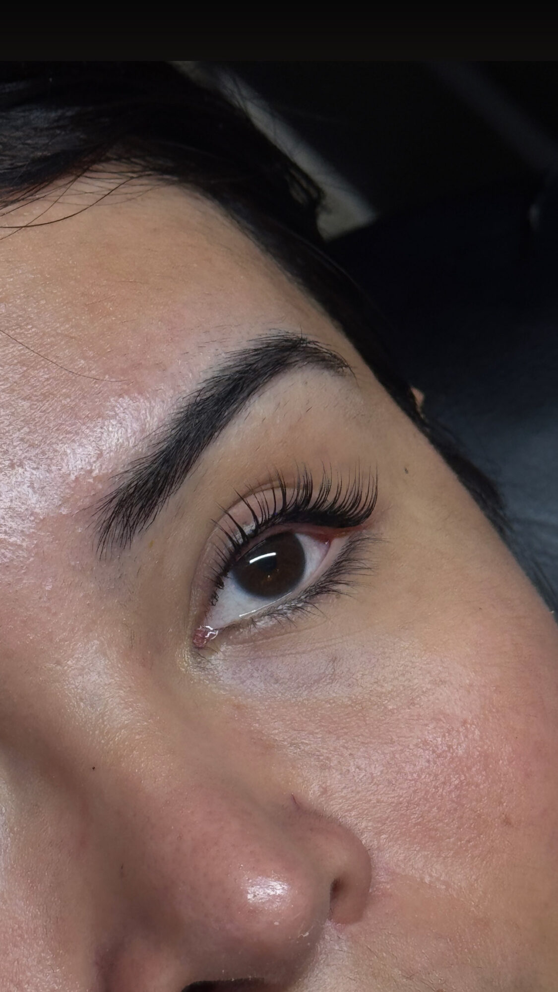 Close-up of a person's eye, eyebrow, and part of the nose with makeup and clear skin.