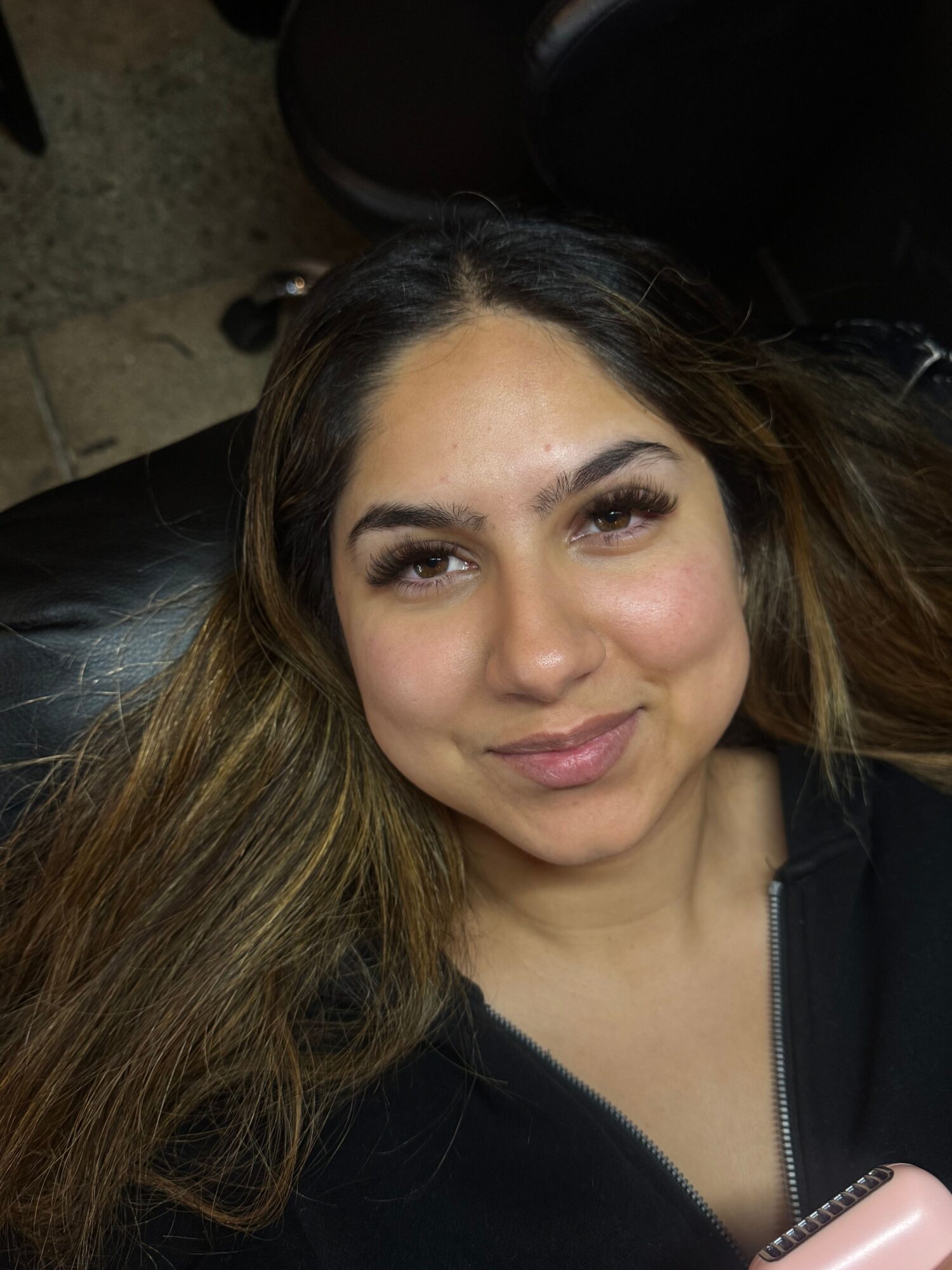 Woman with long hair lying down, eyes closed, wearing a black top, in a close-up shot.