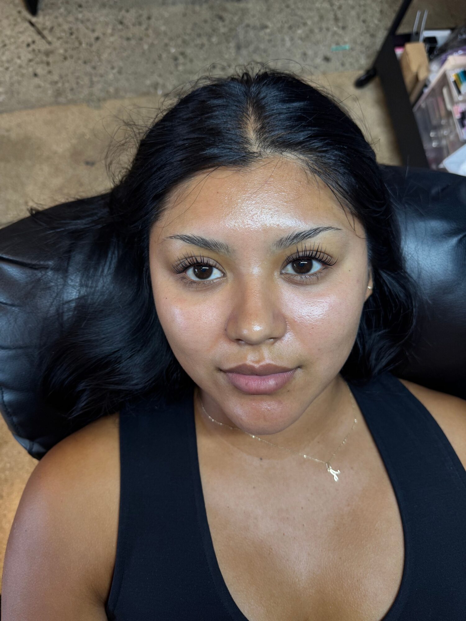 Woman with long black hair lying on a black surface, wearing a black top, looking at the camera.