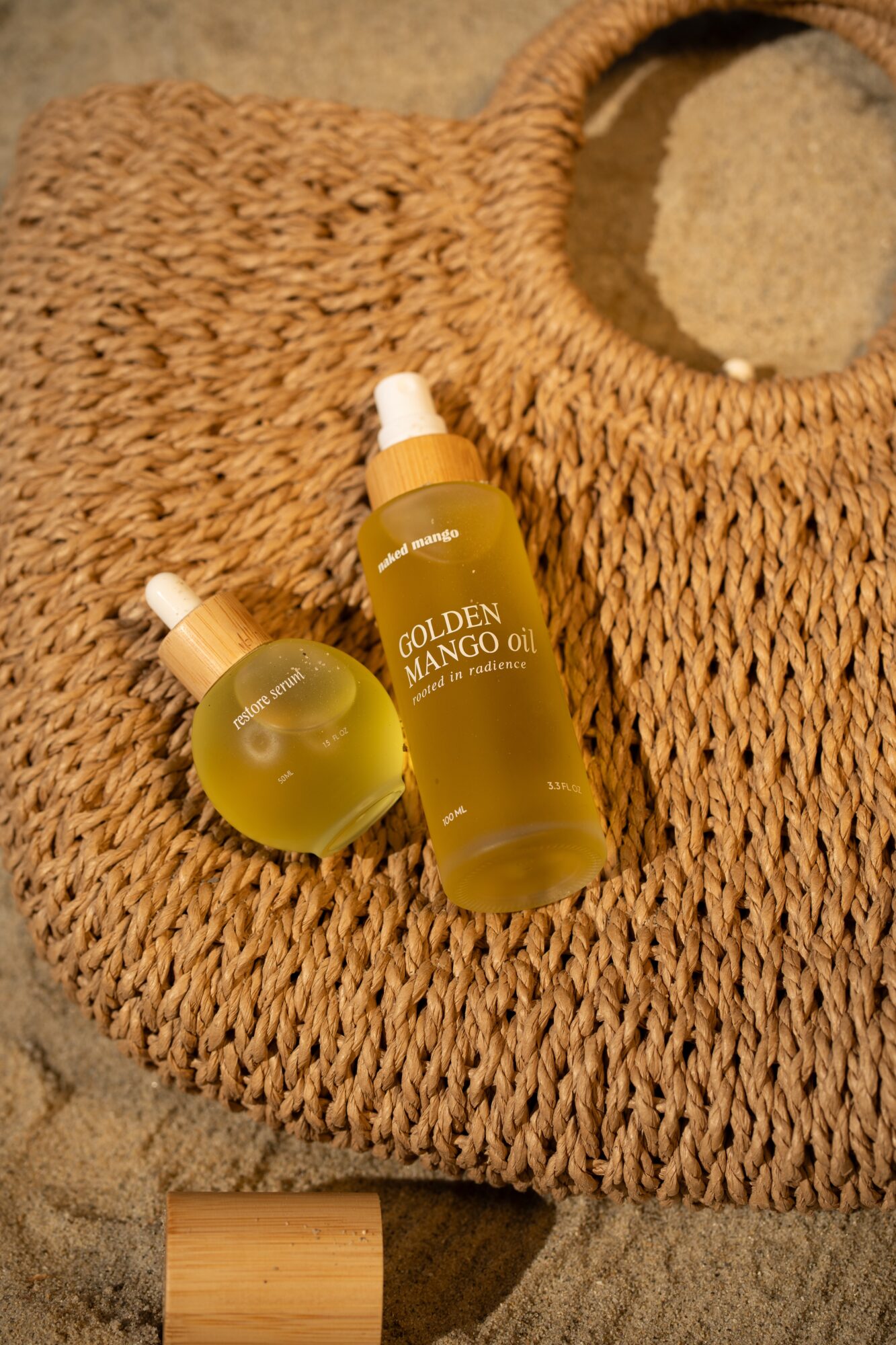 Two golden-colored bottles labeled 'Golden Mango Oil' on a woven circular mat with a mirror in the background.