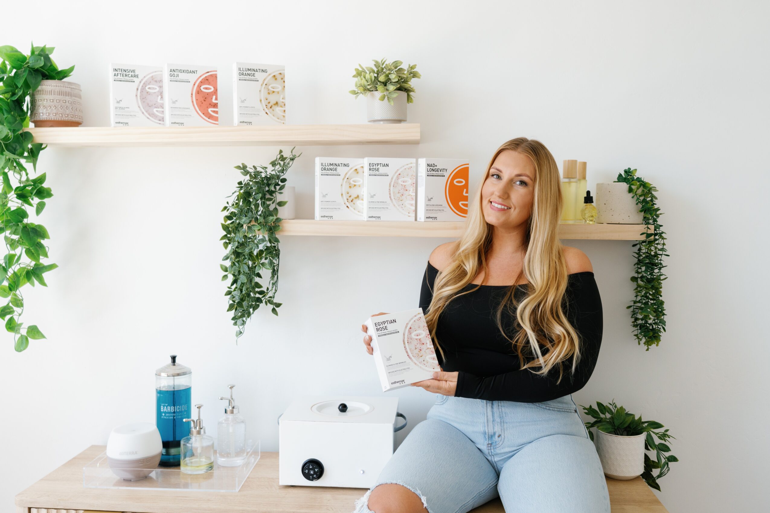 Woman with long blonde hair holding a paper in a bright, minimalistic room with plants and shelves.