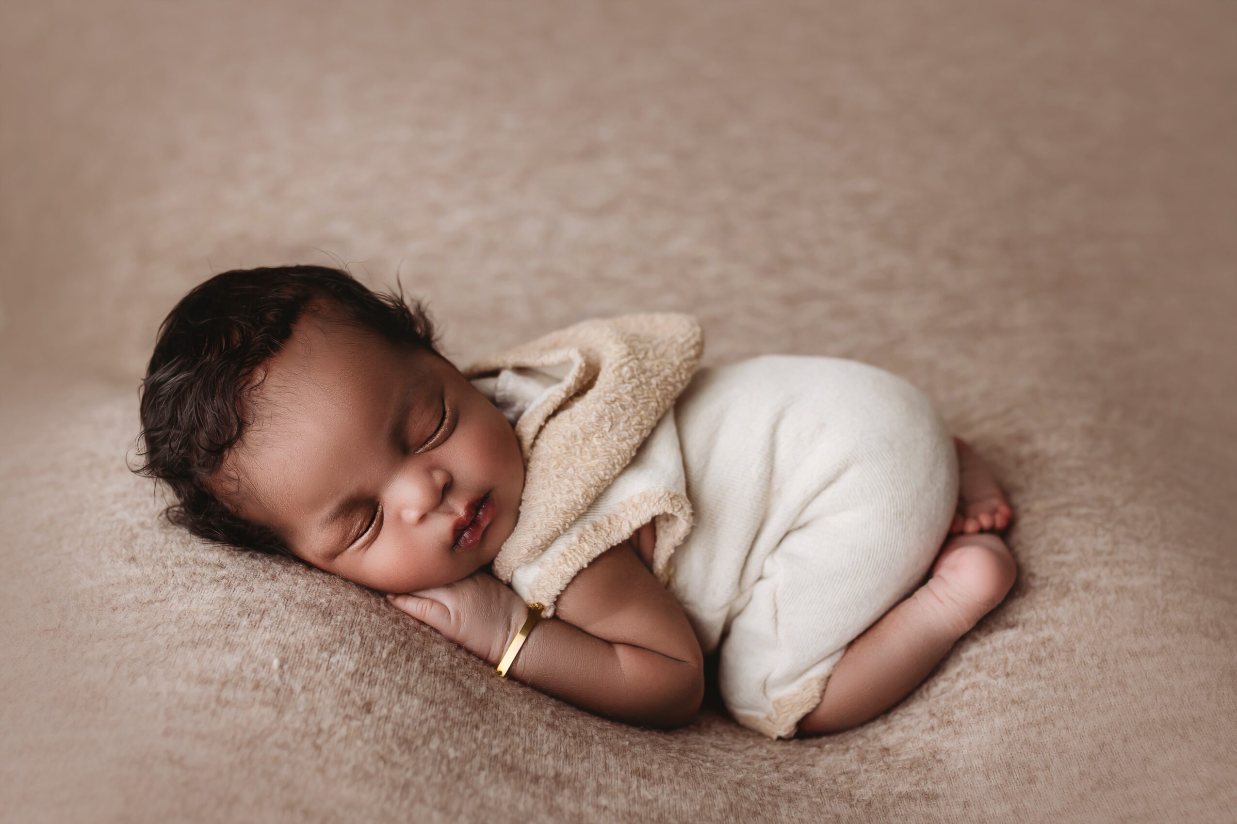 Baby sleeping on side with head resting on hand, wrapped in a blanket, lying on soft surface.