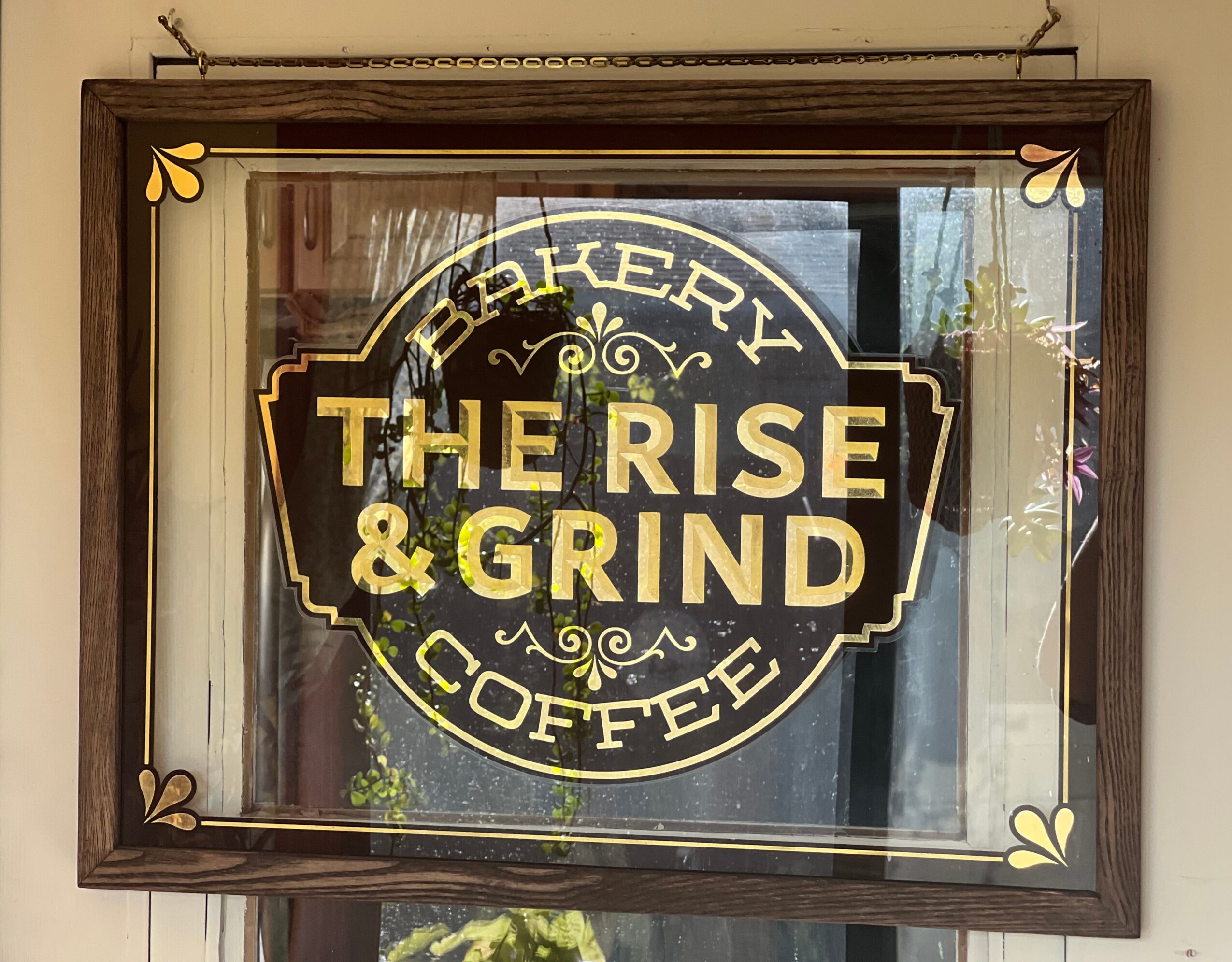 Sign for bakery, coffee, and grind shop with decorative border and text, seen through glass window.
