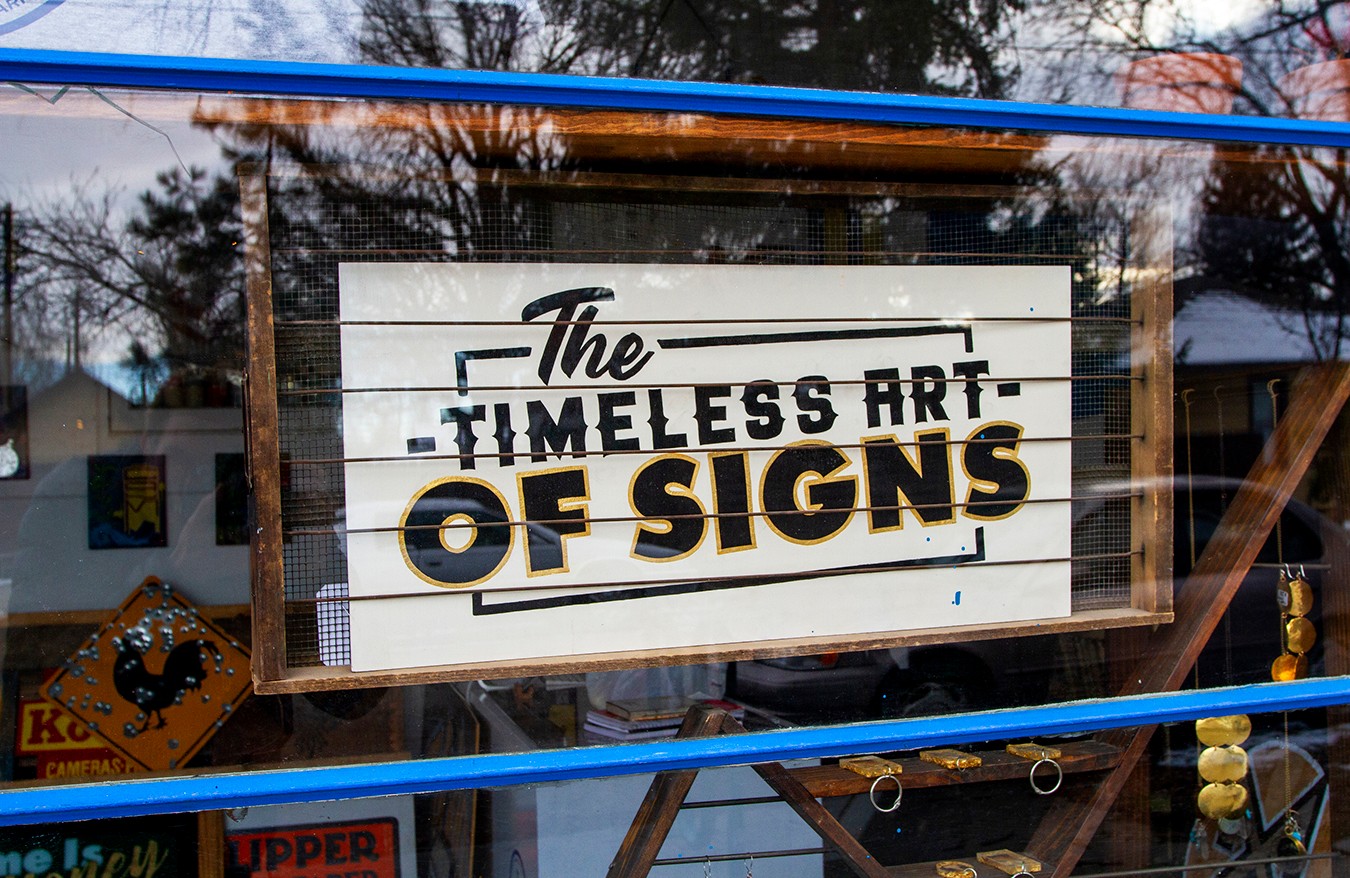 Sign reads 'The Timeless Art of Signs' with black and gold text on a white background.