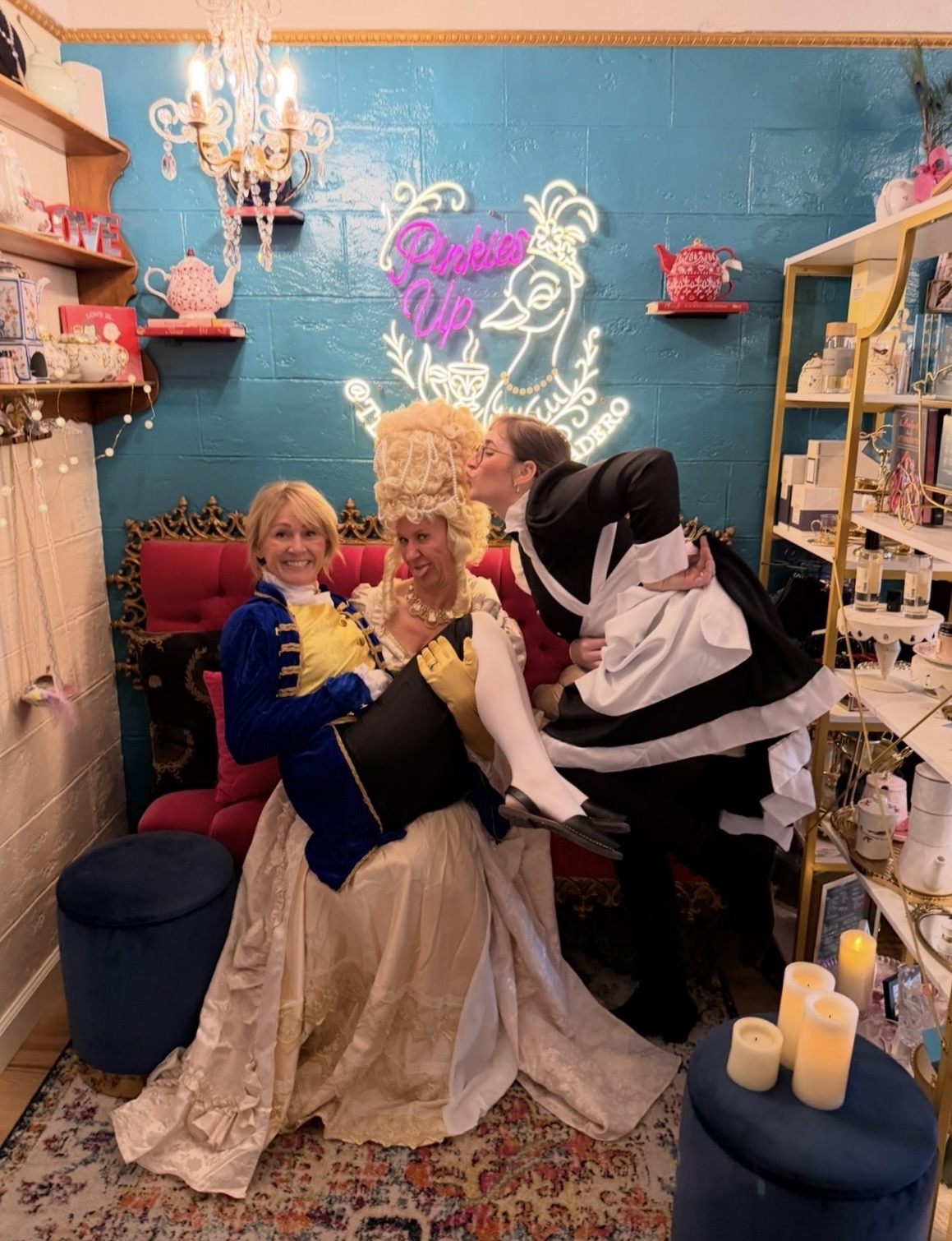 Three people in a boutique, one in a wedding dress, two others with playful expressions, colorful decor, and candles. Word 'Doll' visible.