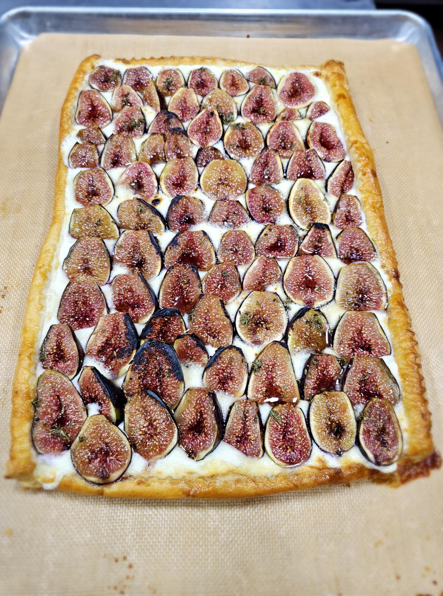 A rectangular pizza topped with sliced figs and cheese, on a beige surface.