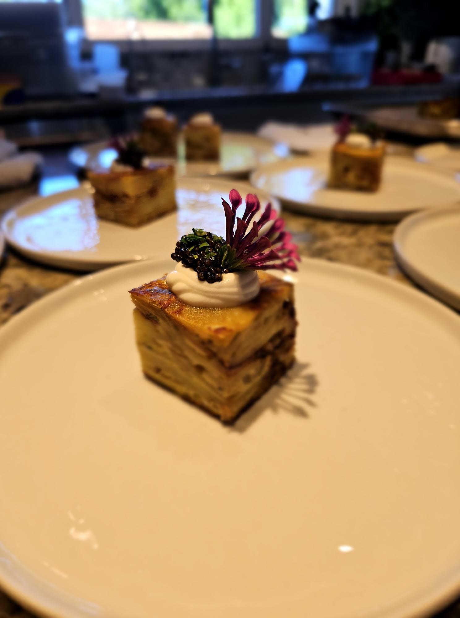 A dessert with a flower and berries on top, served on a wooden block, on a white plate.