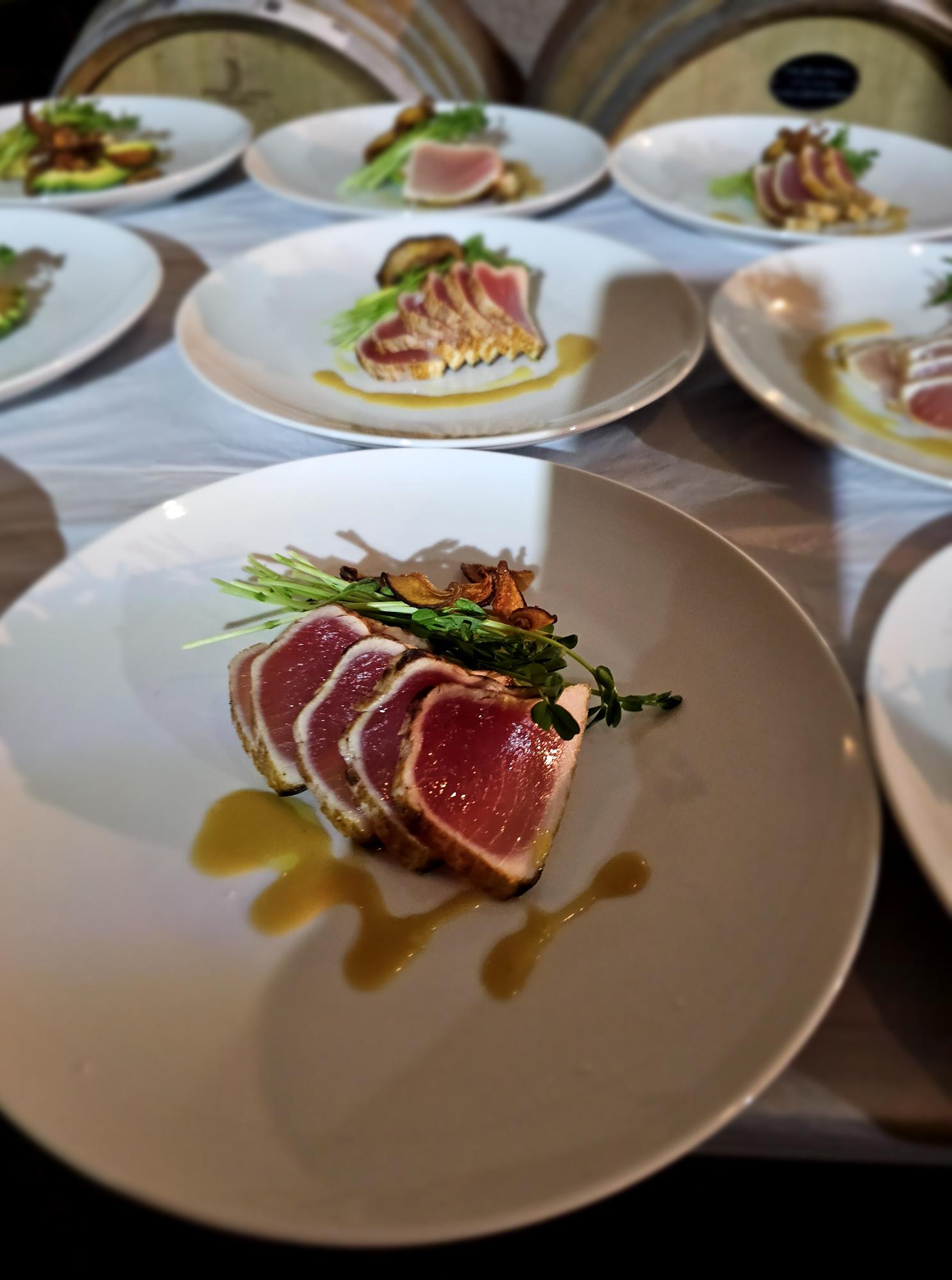 Slices of raw meat with greens and sauce on a white plate, viewed from the side.