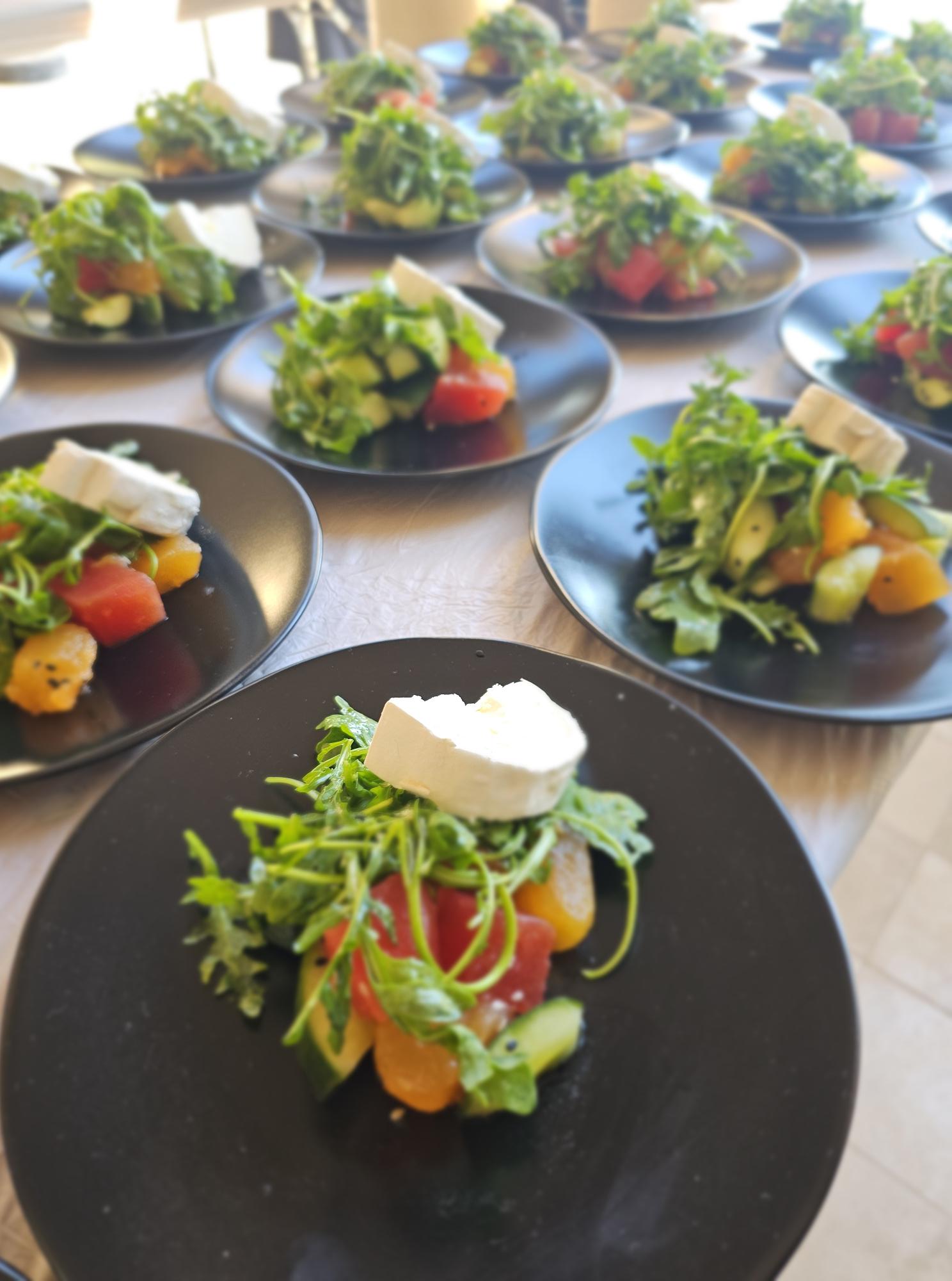 Assorted salads with vegetables and greens on black and white plates, arranged on a table.