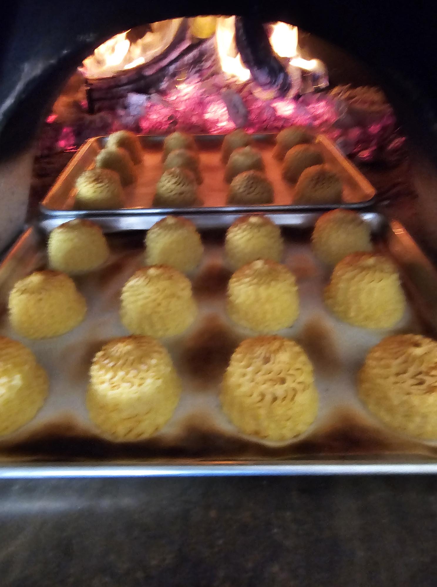 Tray of yellow spherical snacks with textured surface, arranged in rows on a metal surface.