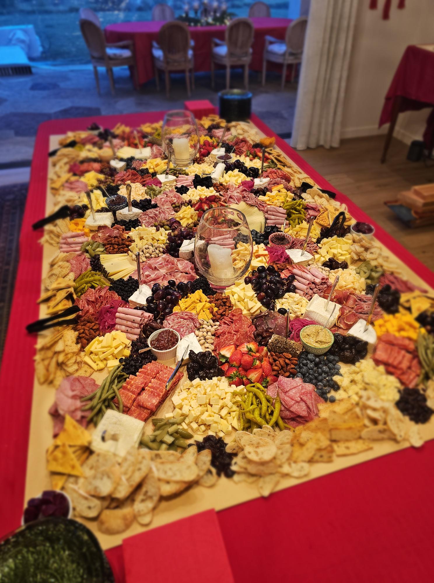 Large triangular fruit and snack platter with various fruits, candies, and snacks on a red tablecloth, viewed from the side.