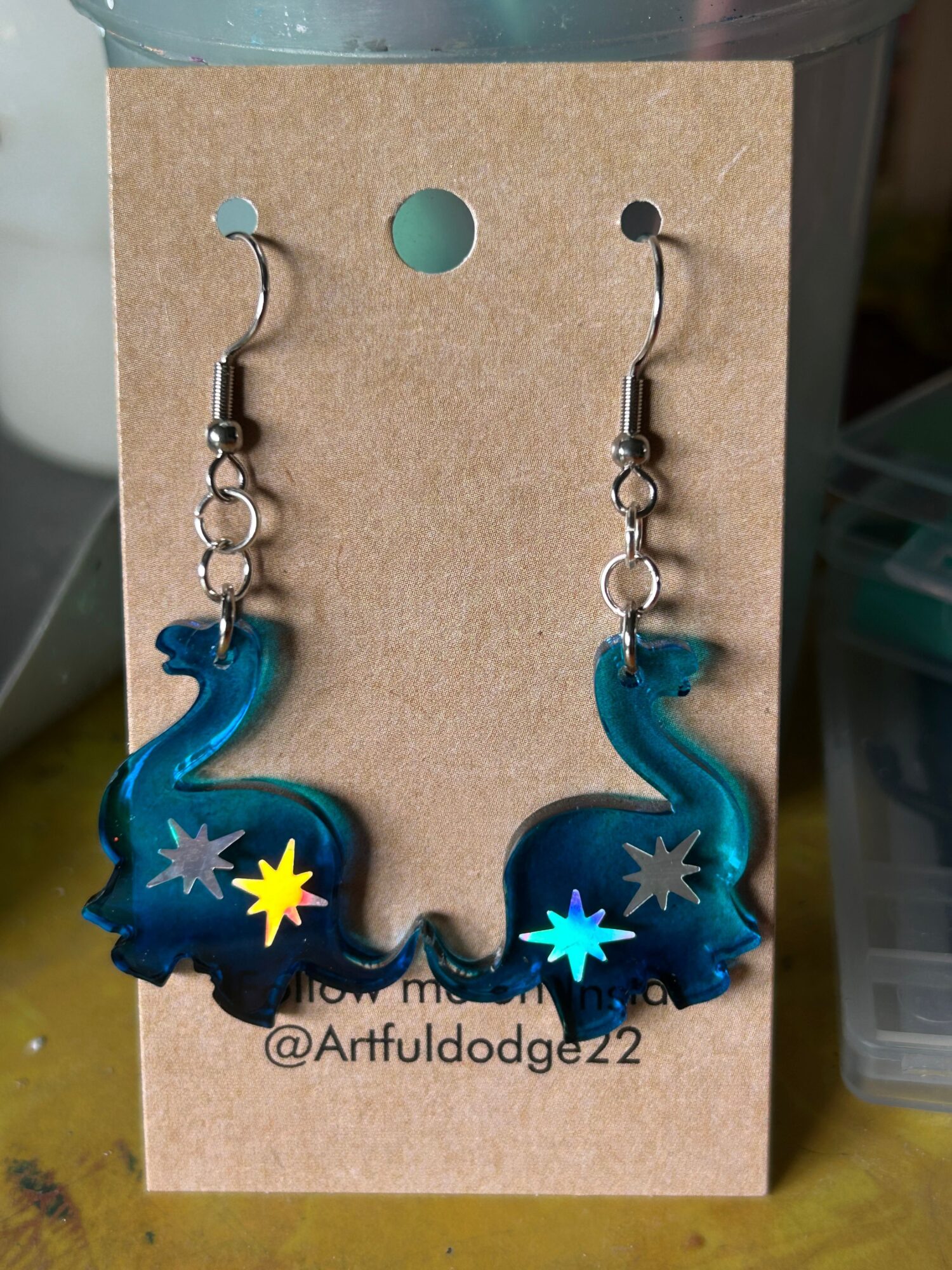 Blue seahorse-shaped earrings with star designs hang on a cardboard backing.