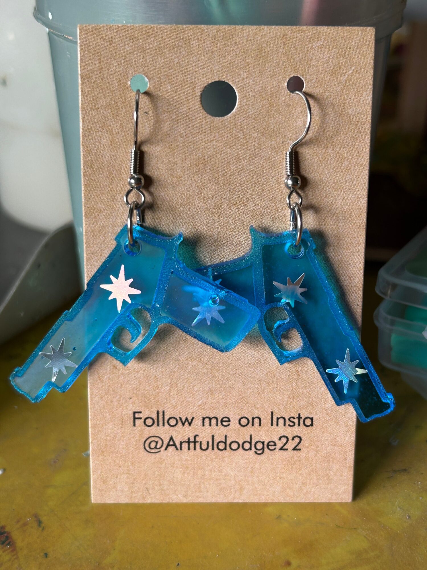 Two blue unicorn-shaped earrings with white star details on a cardboard backing, with a follow Instagram handle. Word count: 20