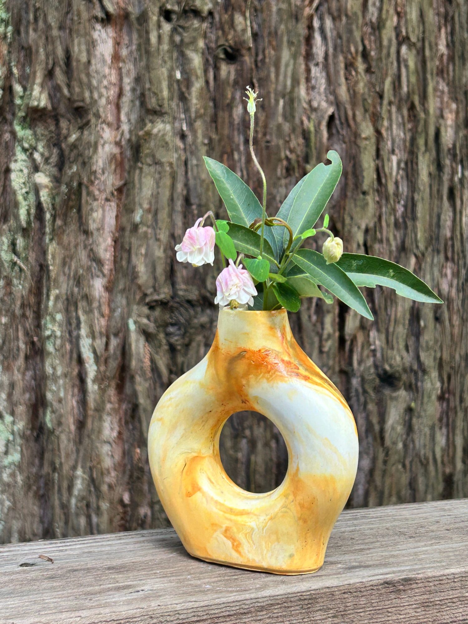 Vase with green leaves and pink flowers on a wooden surface, against a textured wooden background.