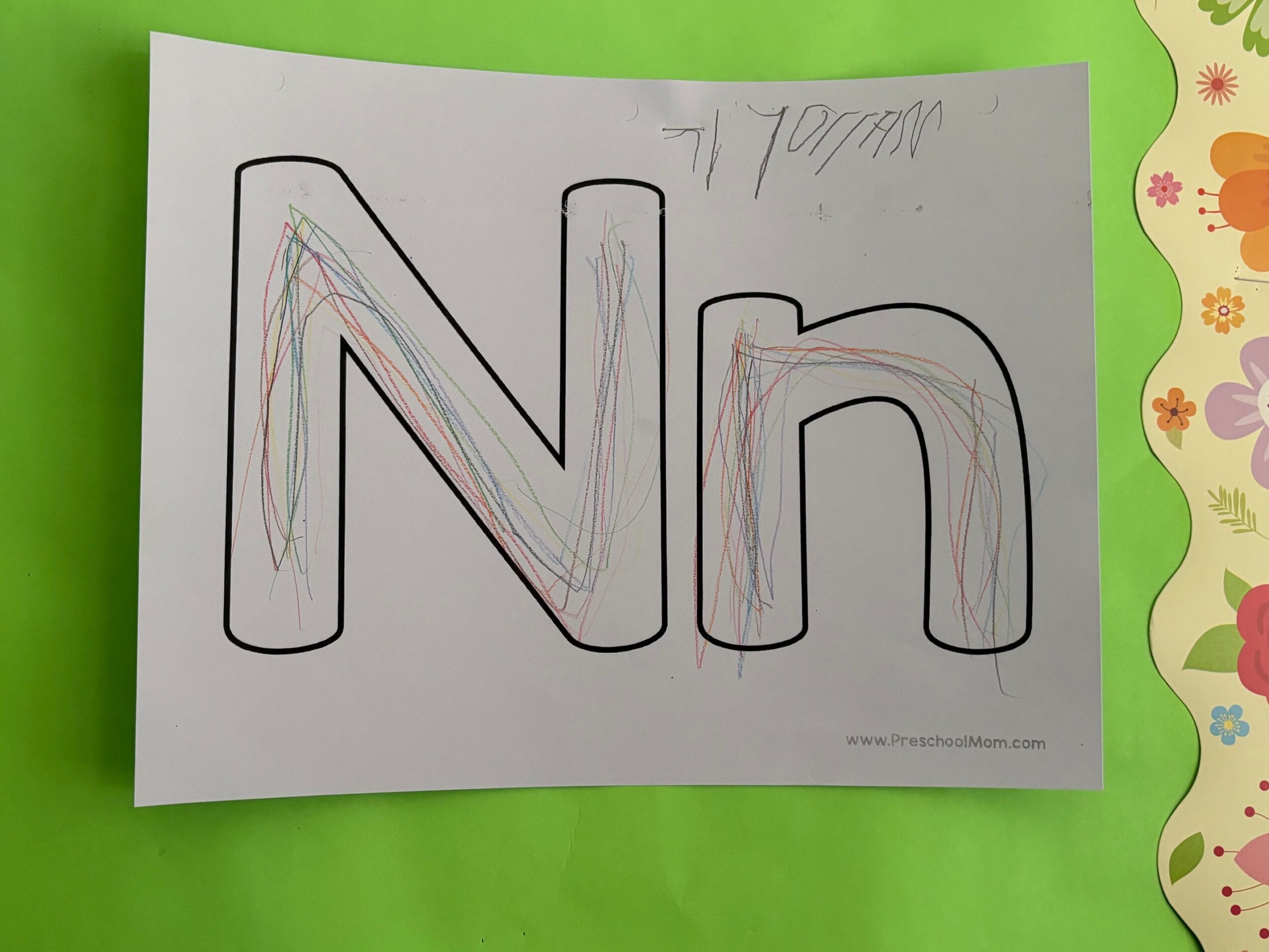 Letter 'N' outlined with colorful scribbles inside, on white paper with a green background.