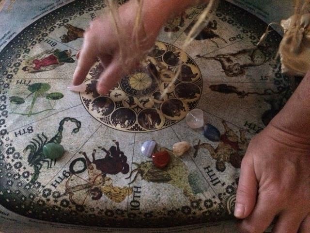 Hands move pieces on a circular zodiac-themed board with astrological symbols and illustrations.