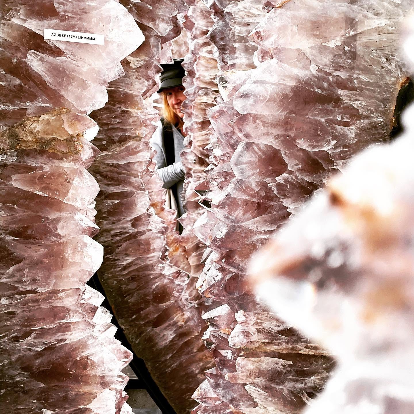Person wearing a hat and coat walking between tall, jagged rock formations in a narrow canyon.
