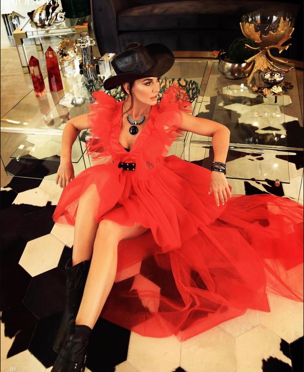 Woman in red dress and black hat sitting on floor with a black and white tiled floor background.