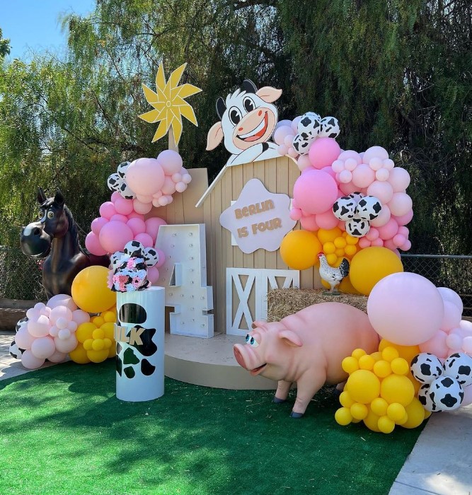 Decorative farm-themed birthday setup with a pig, cow, and cow-themed balloons, featuring a smiling cartoon cow and a star, outdoors.