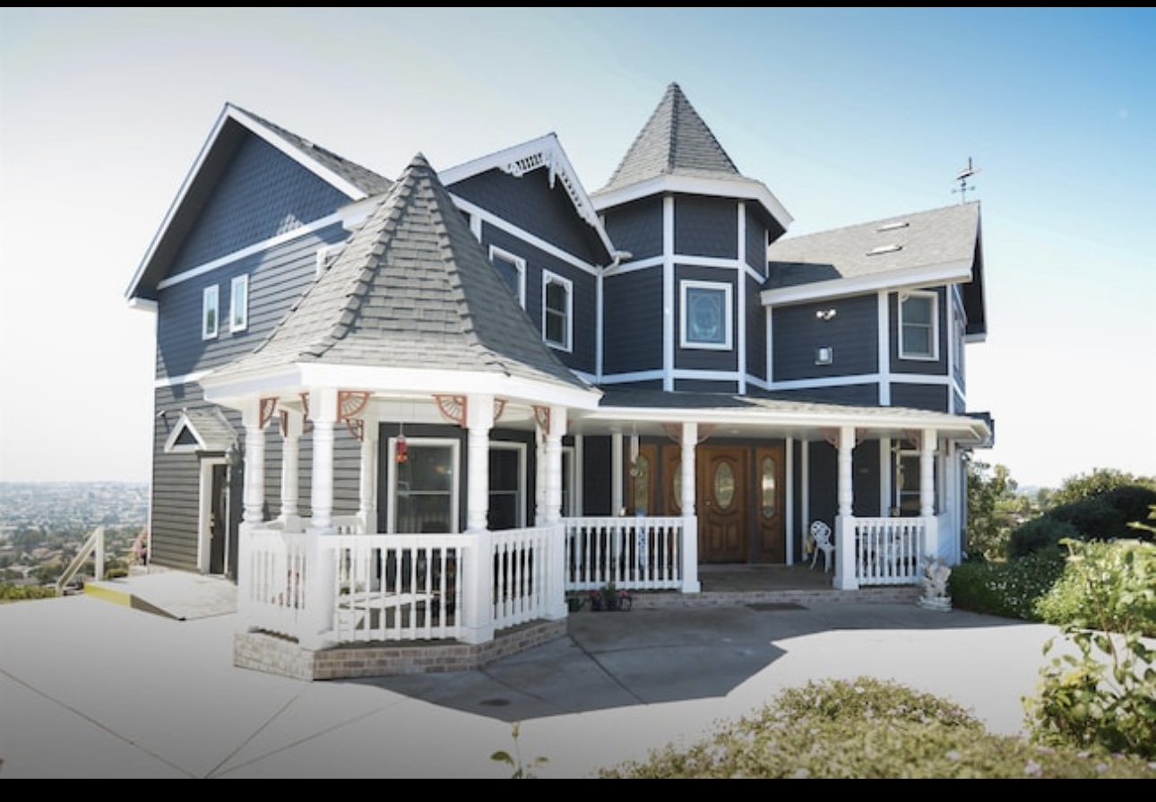 Large blue Victorian-style house with multiple turrets, white trim, and a front porch, set against a clear sky.