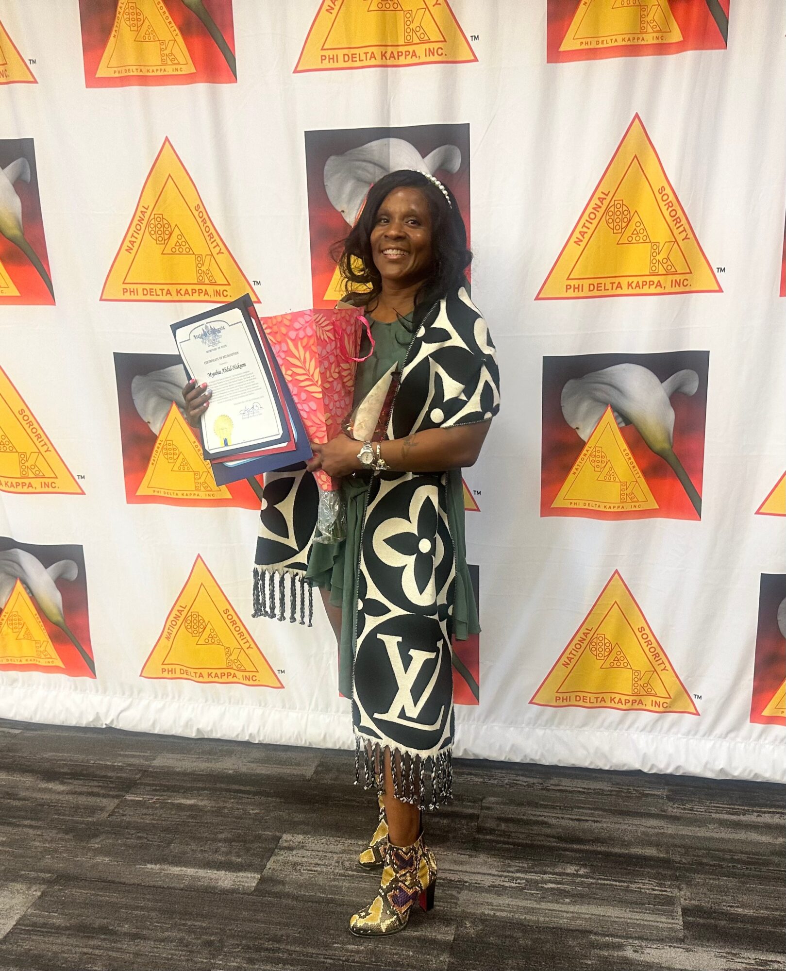 Woman holding a framed certificate and bouquet, standing in front of a backdrop with warning triangle and shark images, smiling.