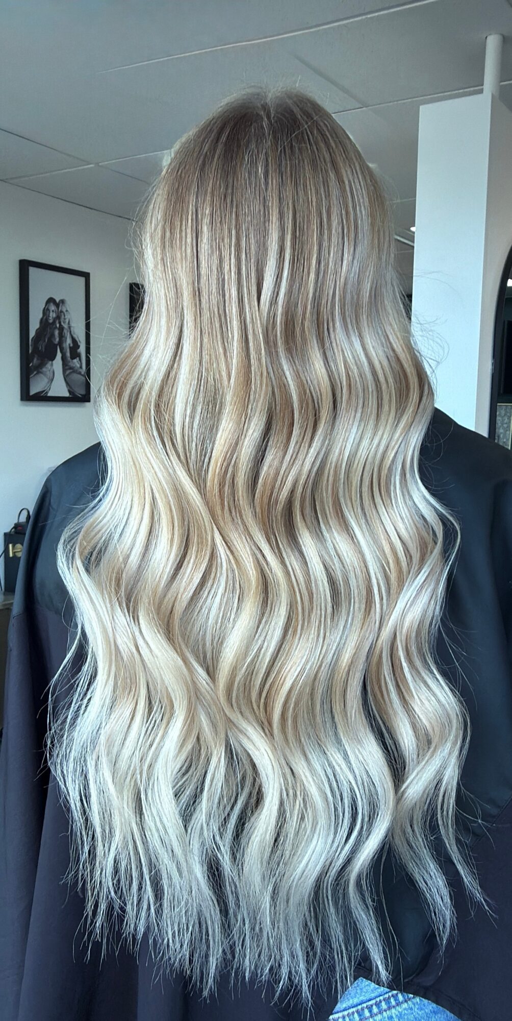 Long wavy blonde hair with darker roots, flowing down the back of a person wearing a black top.