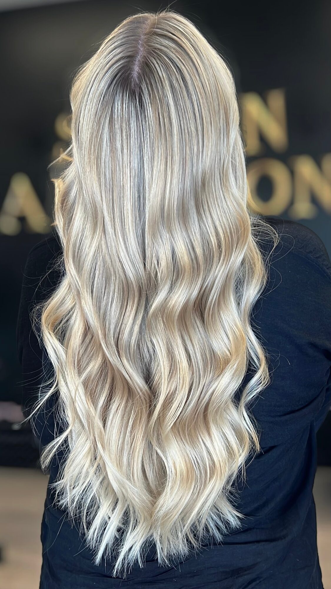 Back view of long, wavy, blonde hair with darker roots, flowing over shoulders.