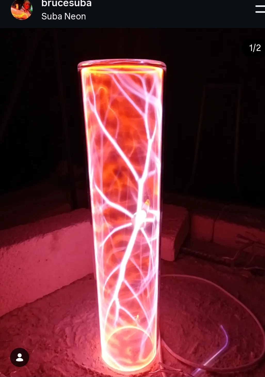 Tall cylindrical neon light with red and white glowing streaks inside, standing on a surface in a dark room.