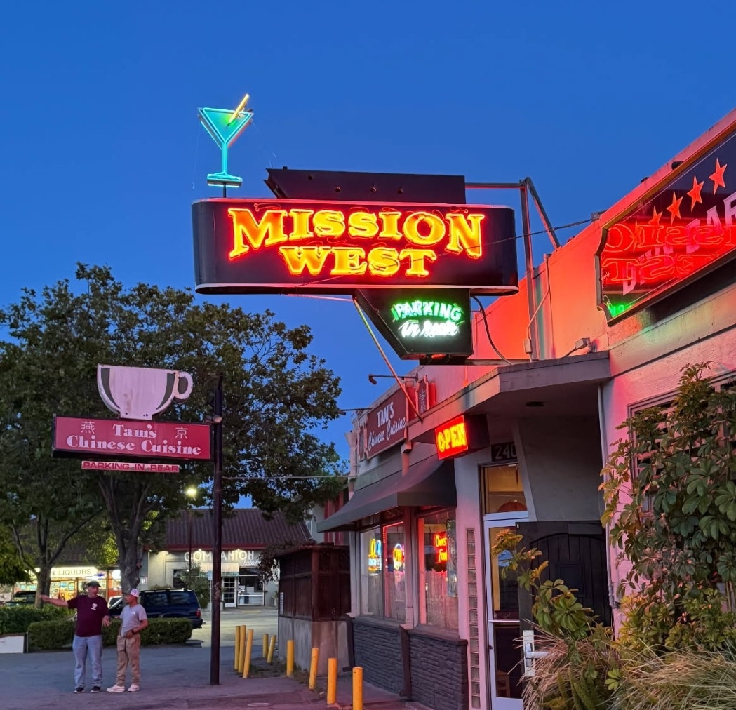 Night scene of a restaurant with neon signs, including 'Mission West' and 'Chinese Cuisine,' with people standing outside.