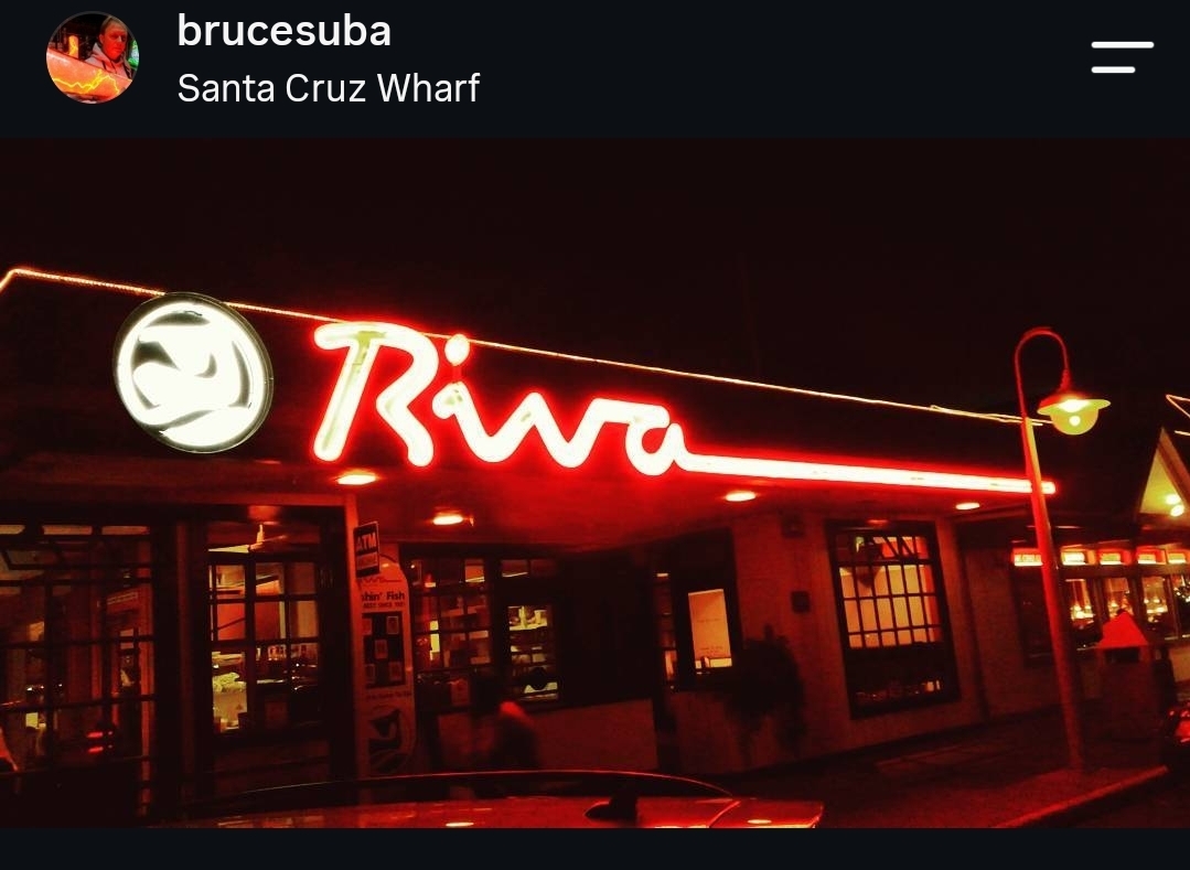 Neon sign reading 'Riwa' above a building with windows and outdoor lighting at night.