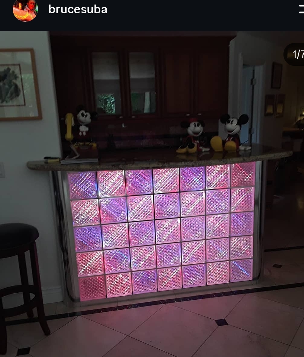 Bar with illuminated pink and purple tiled front, Mickey Mouse figurines on top, wooden cabinets in background, and a stool nearby.