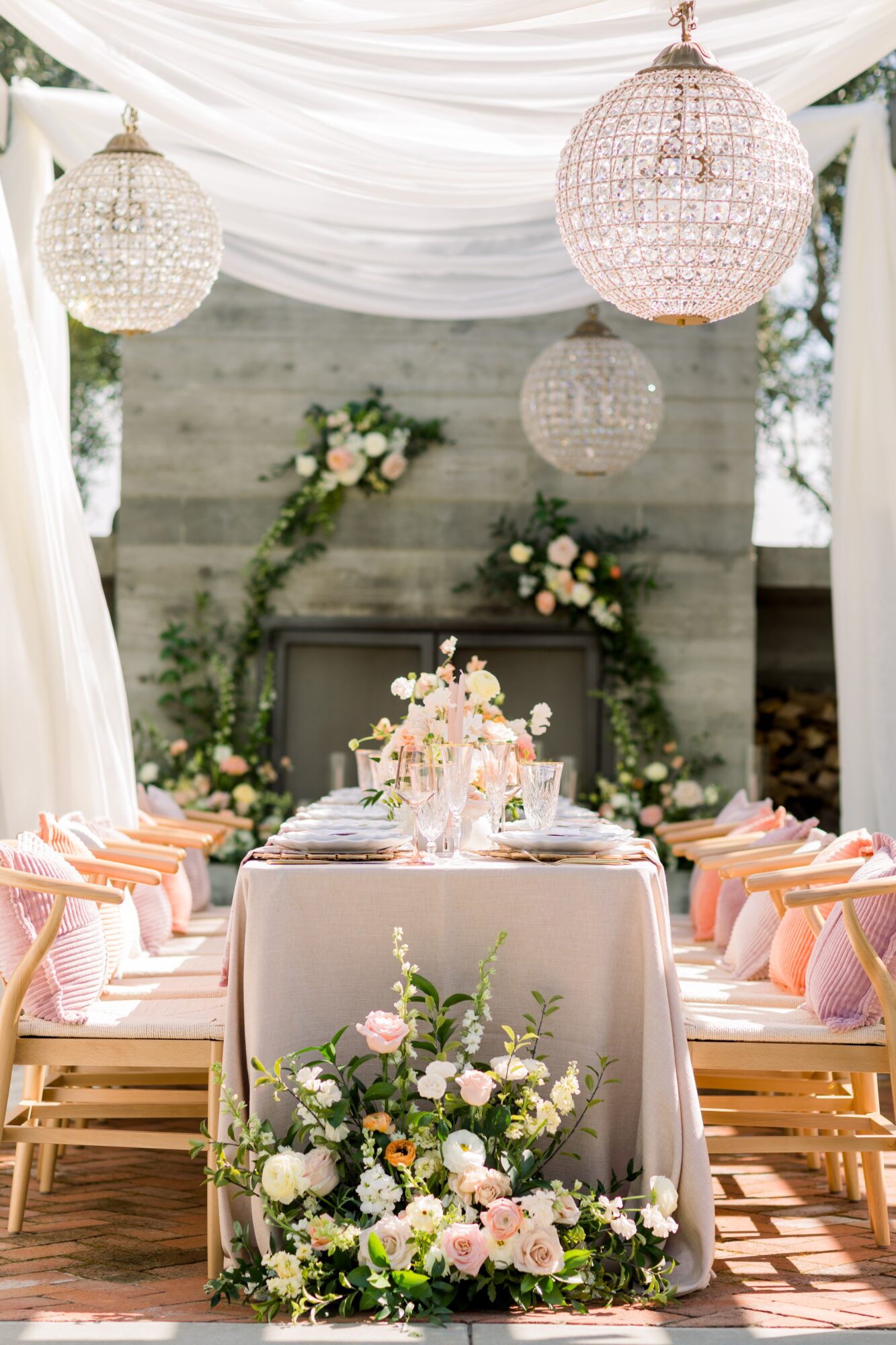 Elegant table setup with floral arrangements, pink chairs, and hanging chandeliers in a decorated indoor space.