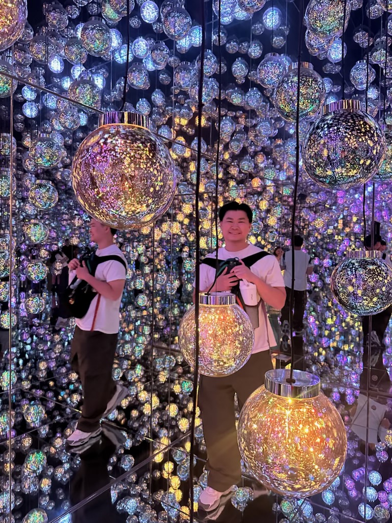 Person standing among illuminated spherical decorations and light displays, with colorful reflections and patterns around them.