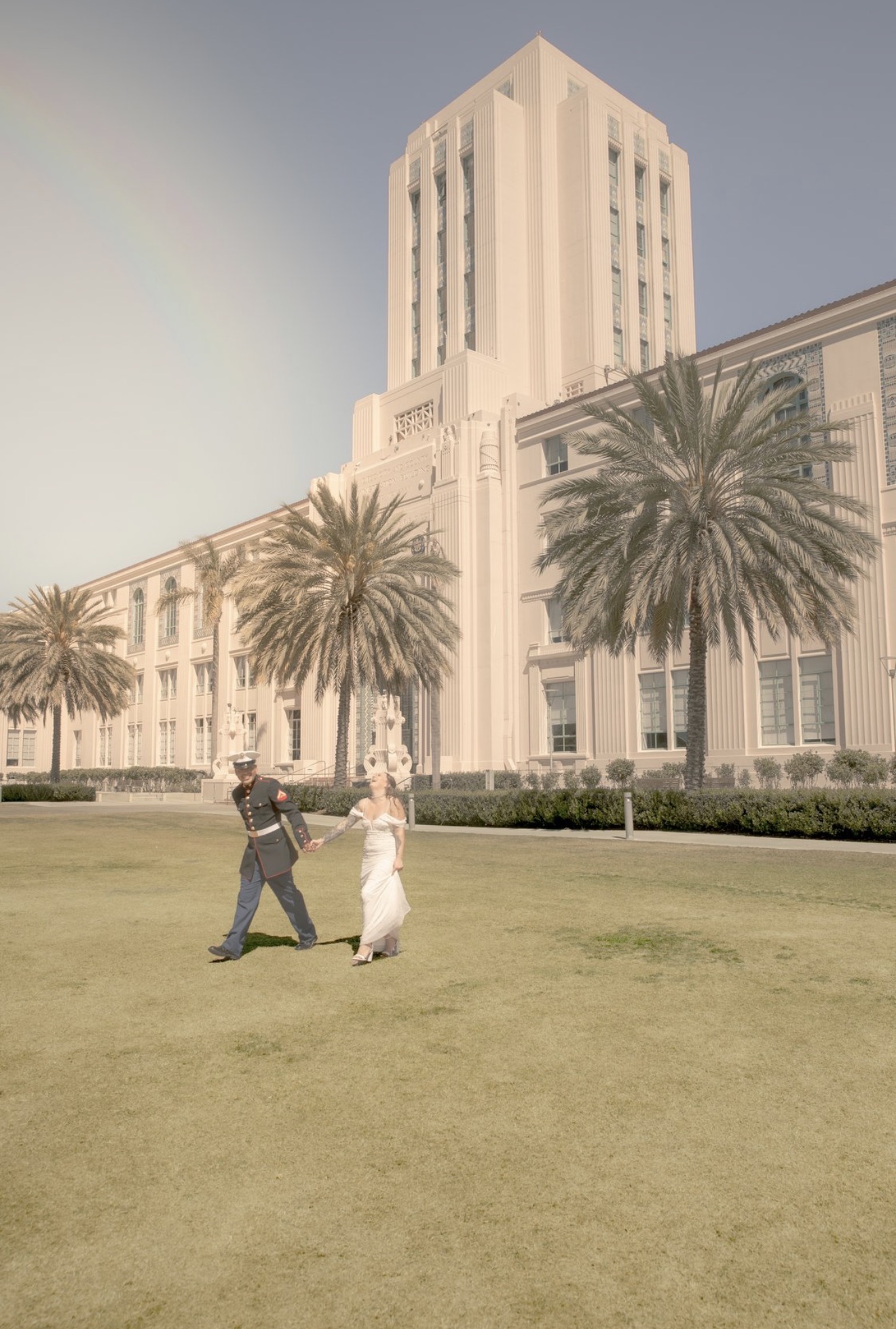 Two people dancing on a grassy area with a large building and palm trees in the background.