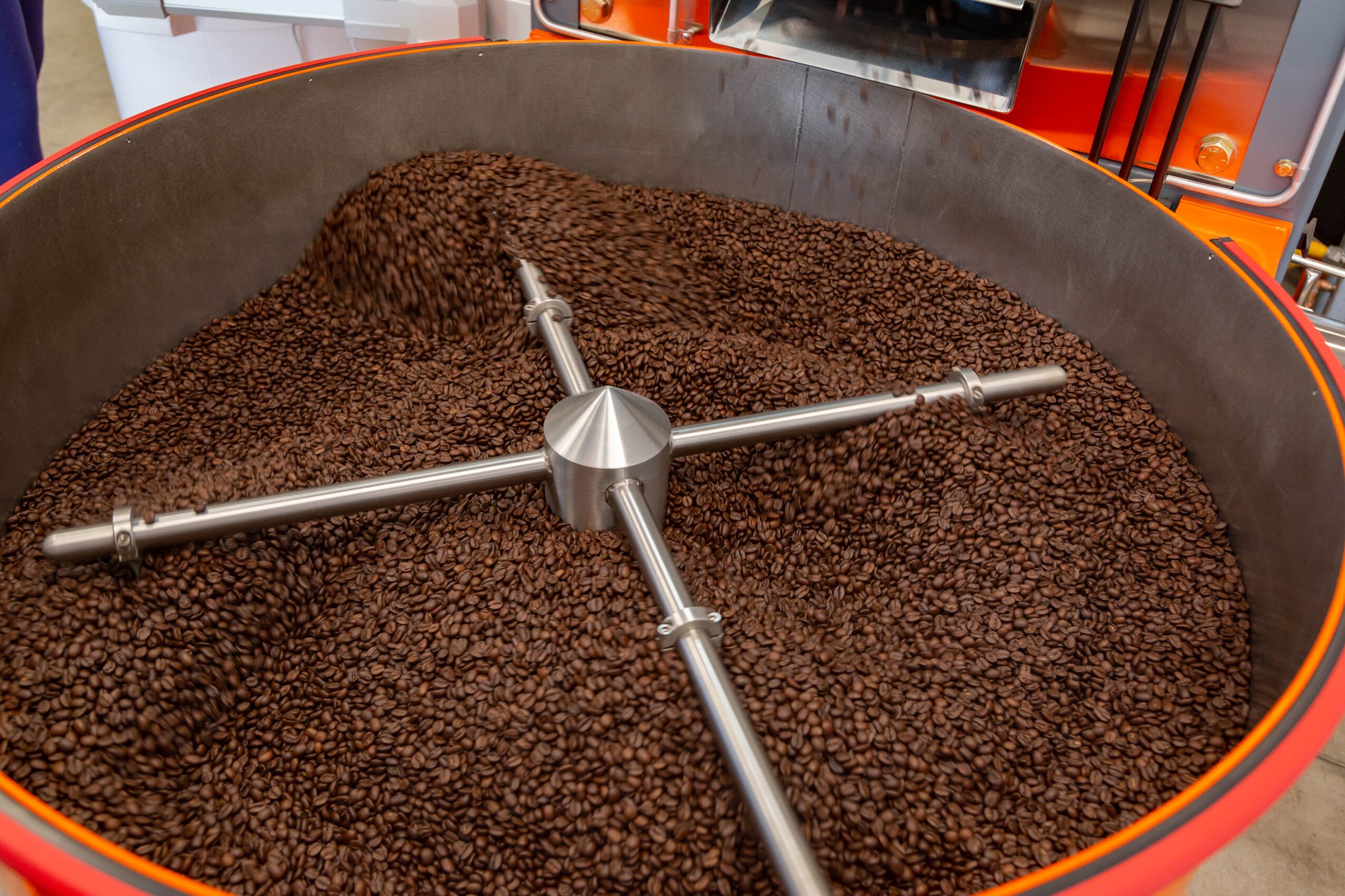 Large container filled with roasted coffee beans, with a metal arm in the center, at a coffee roasting facility.