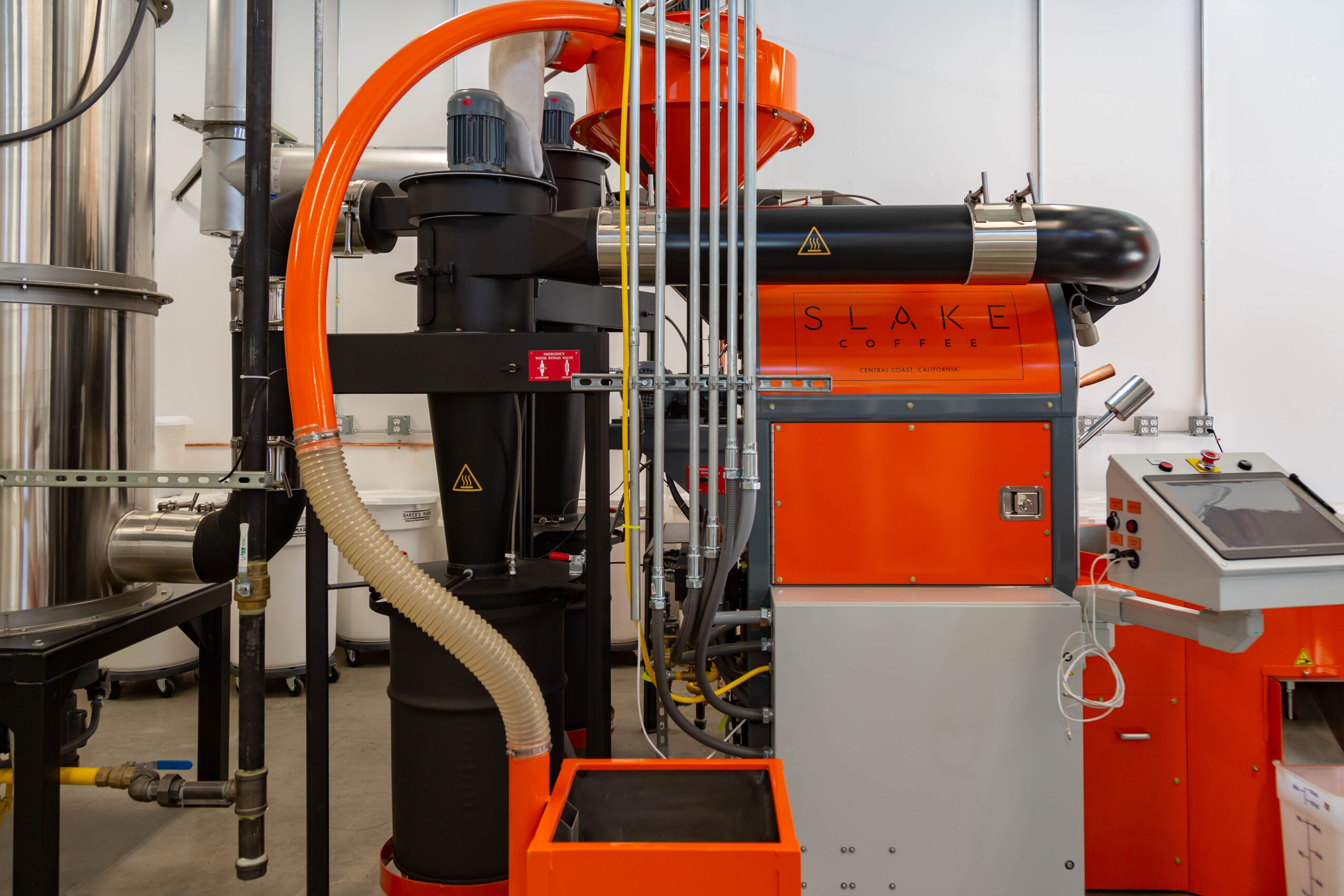 Industrial equipment with black, orange, and gray components, including pipes, tubes, and control panels, in a factory setting.