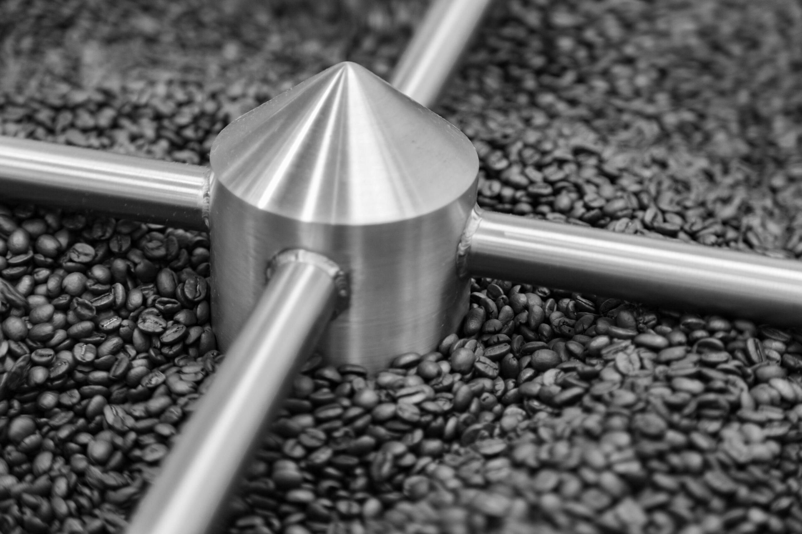 Close-up of a metallic object with four arms on a textured surface of small black stones.