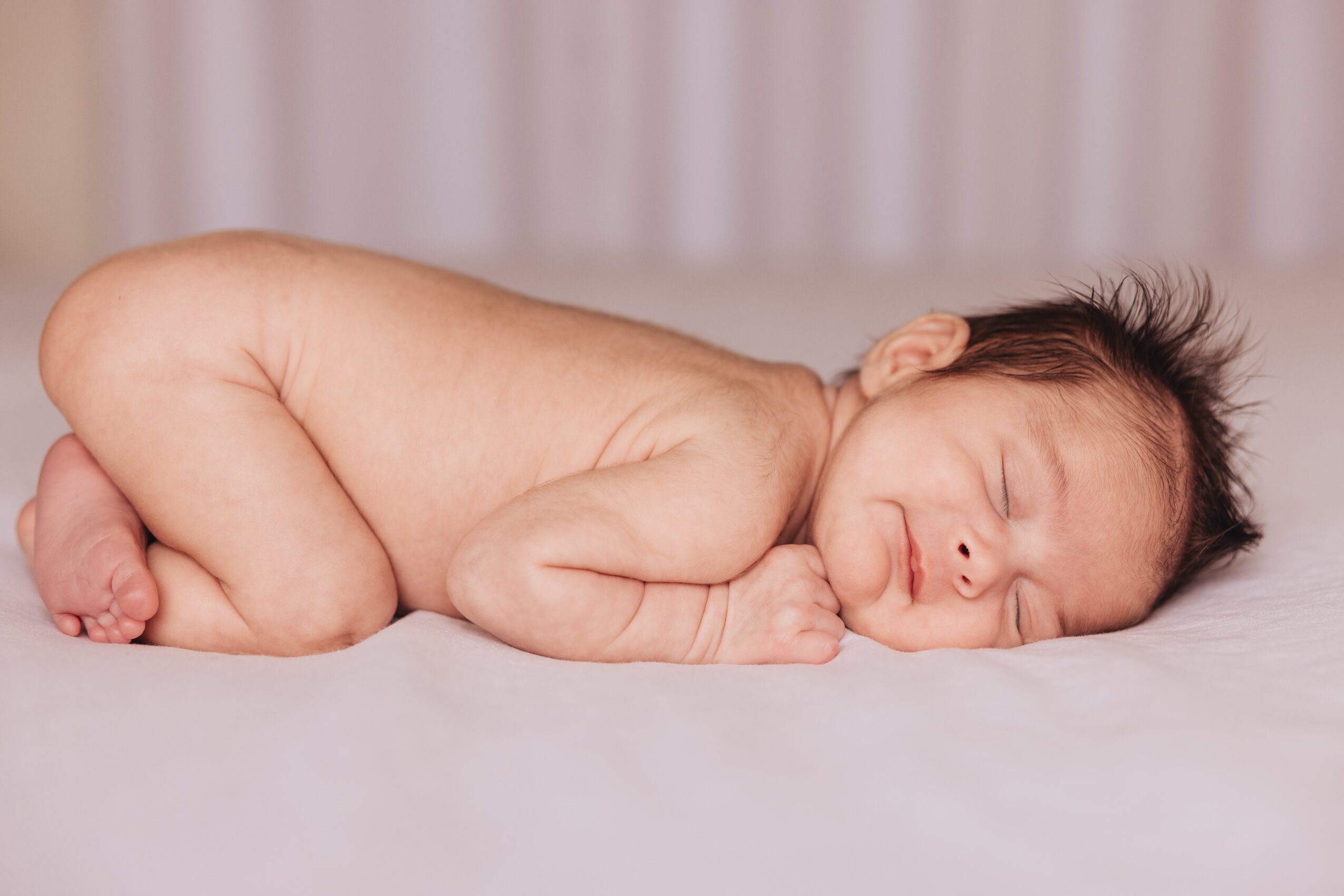 Sleeping newborn baby lying on side with head resting on hands, on a soft surface, background with curtains